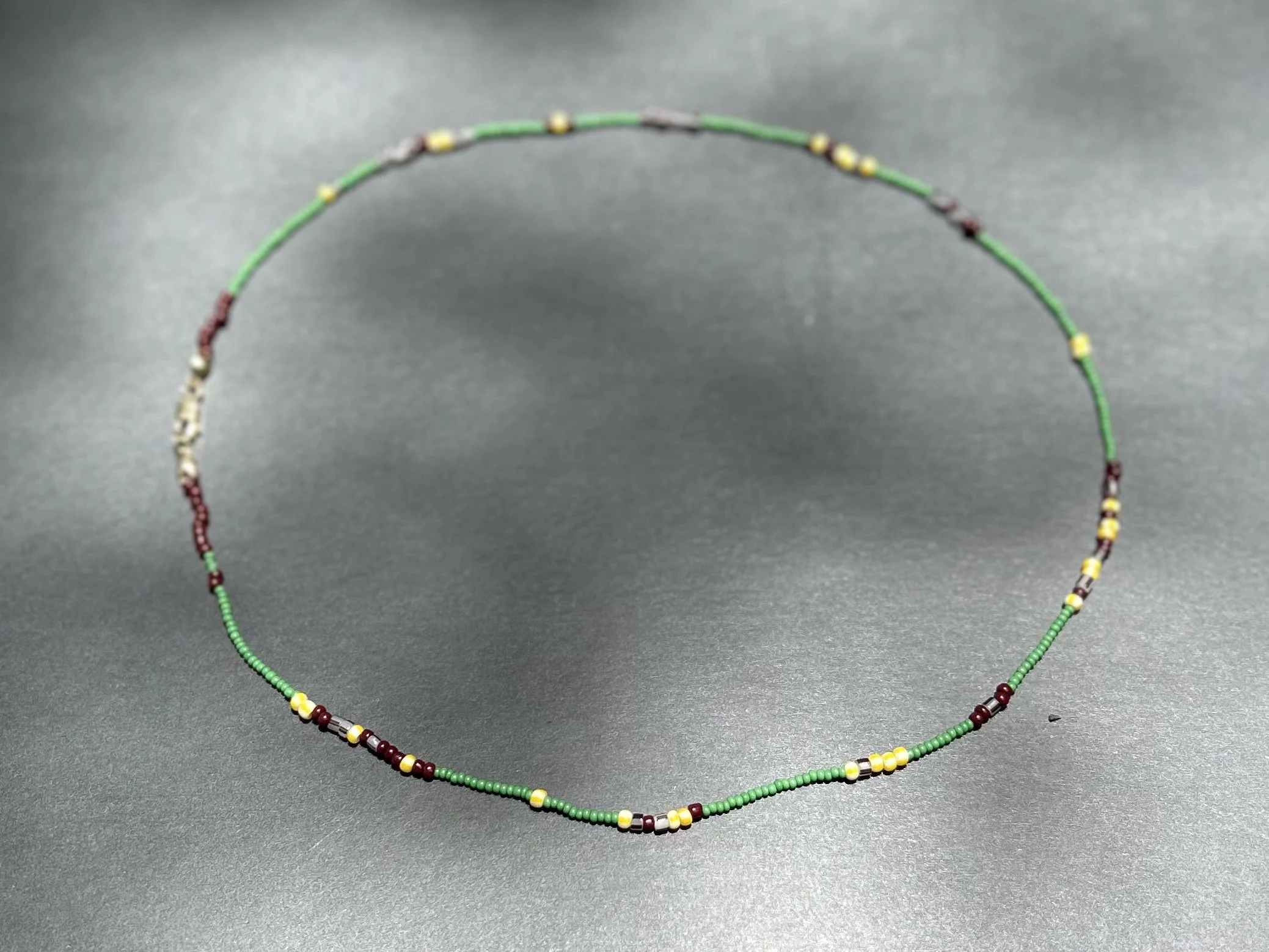 Colorful beaded necklace with green, yellow, maroon, and white beads, laid on a gray surface.