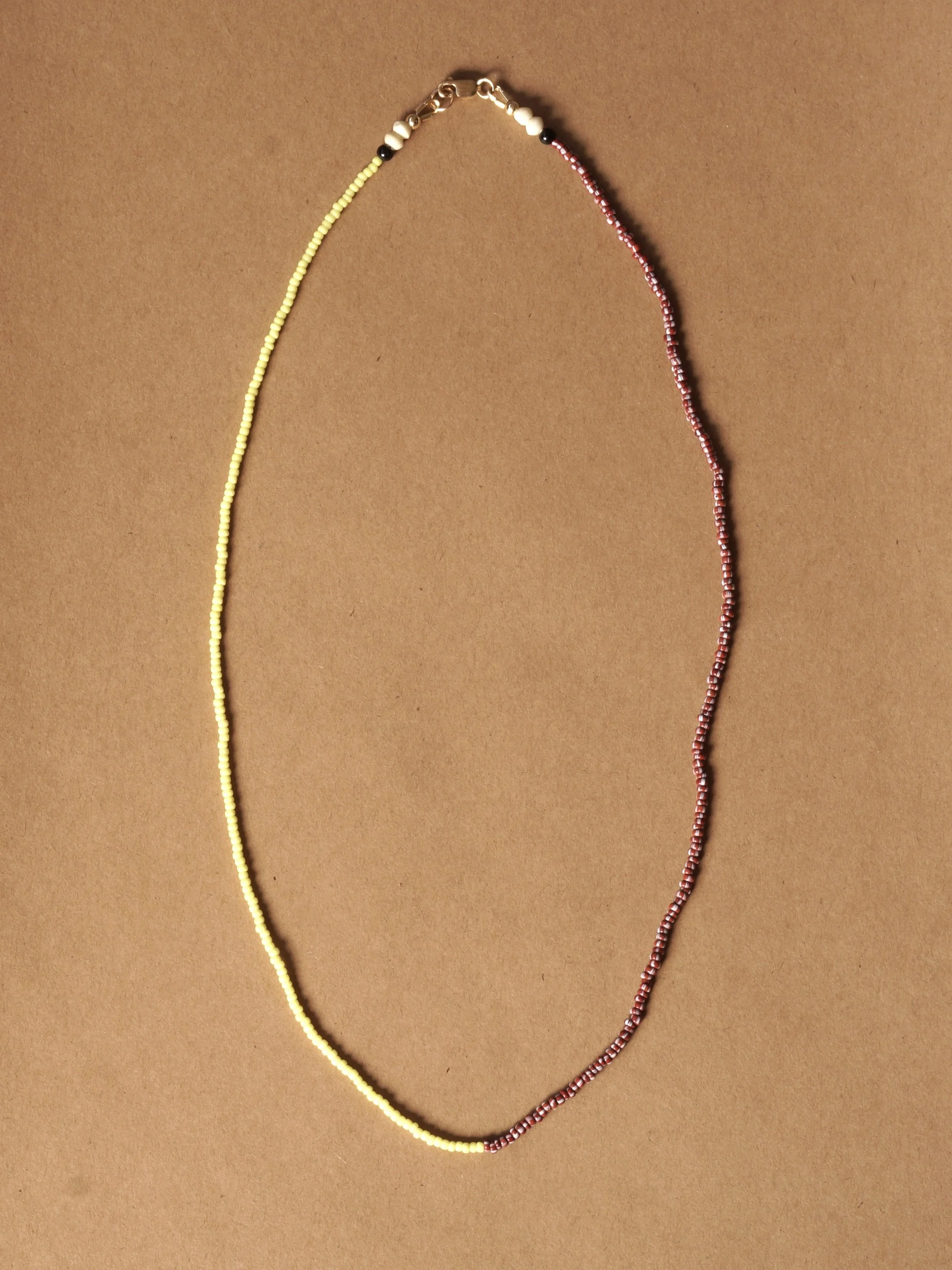 A beaded necklace with sections of yellow beads on one side and red beads with white accents on the other, laid out on a brown background.