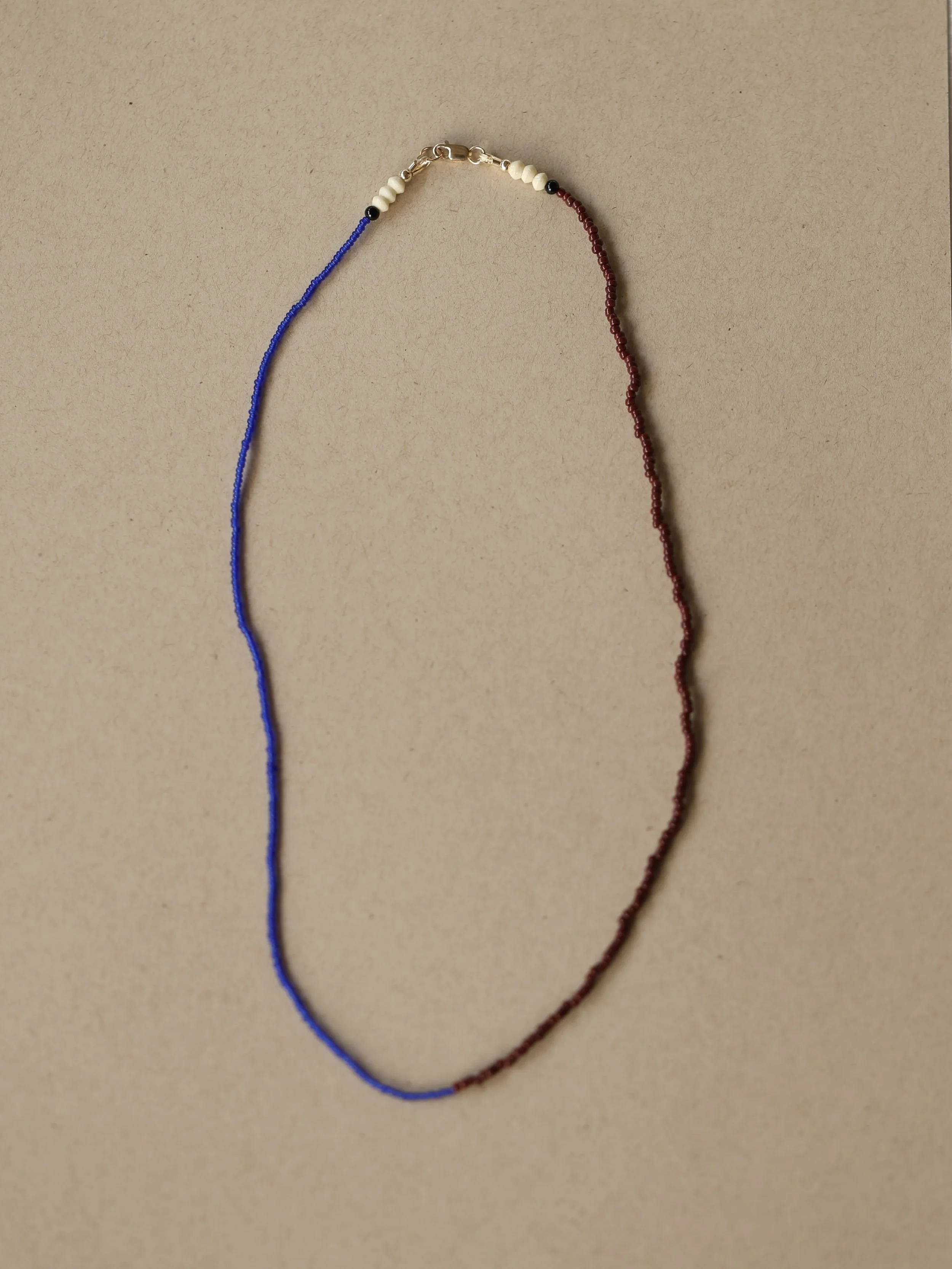 Two strands of beads, one blue and one red, each with small white and black spacer beads, connected at one end with a metal clasp on a beige background.