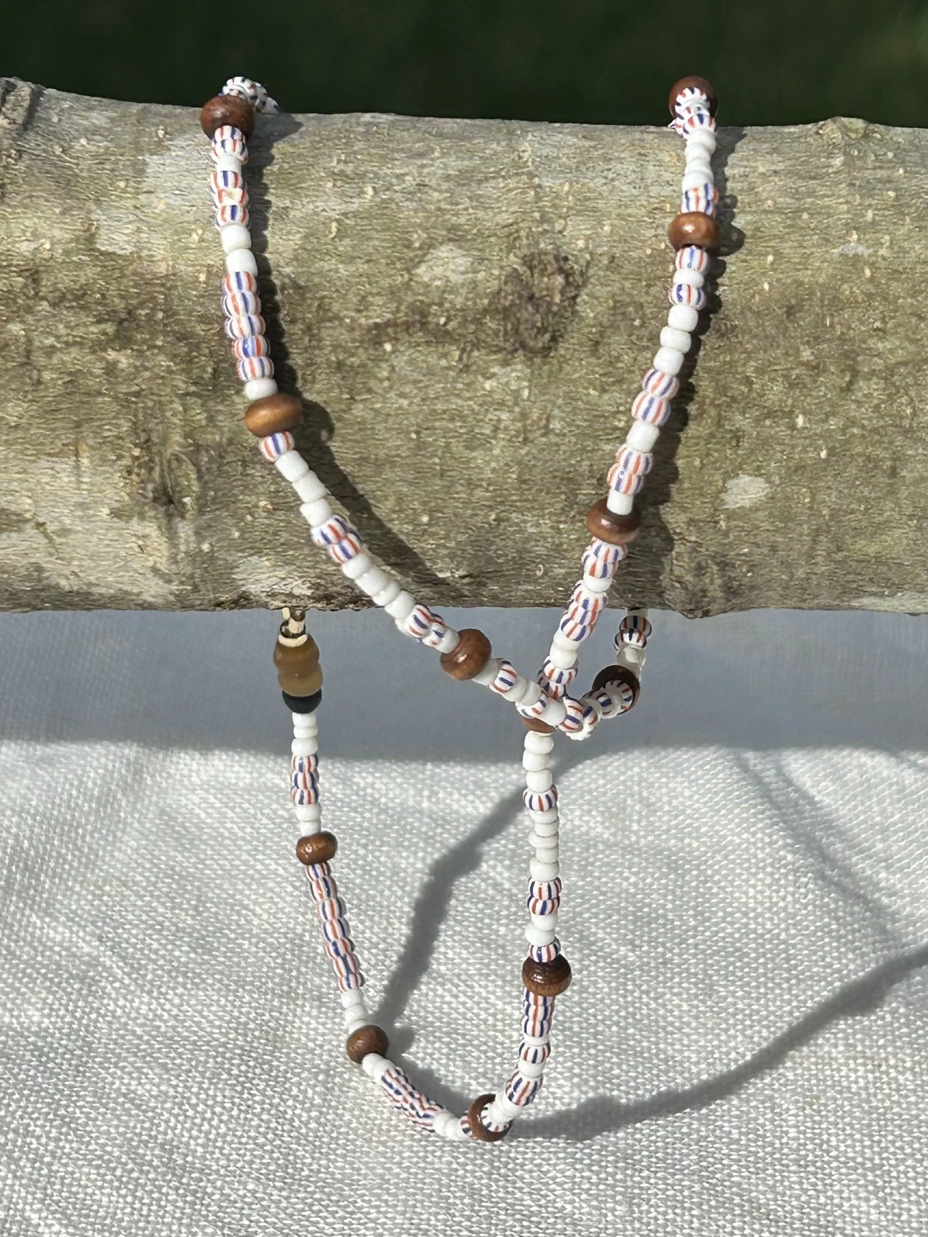 Beaded necklace with white, brown, and striped beads hanging on a piece of wood.