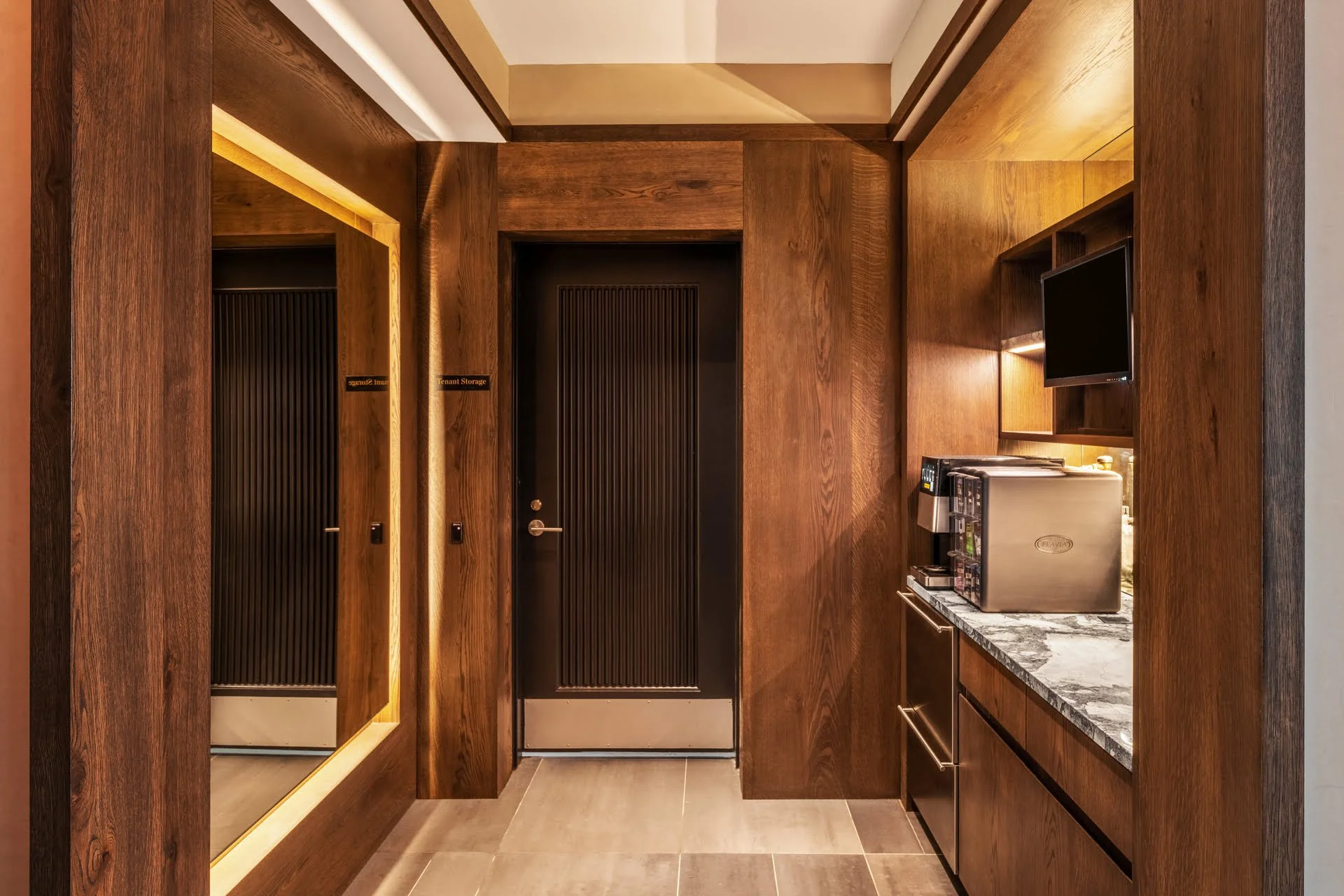 A small kitchen or bar area with wooden cabinets and walls, a stone countertop, a mini refrigerator, and a coffee machine.
