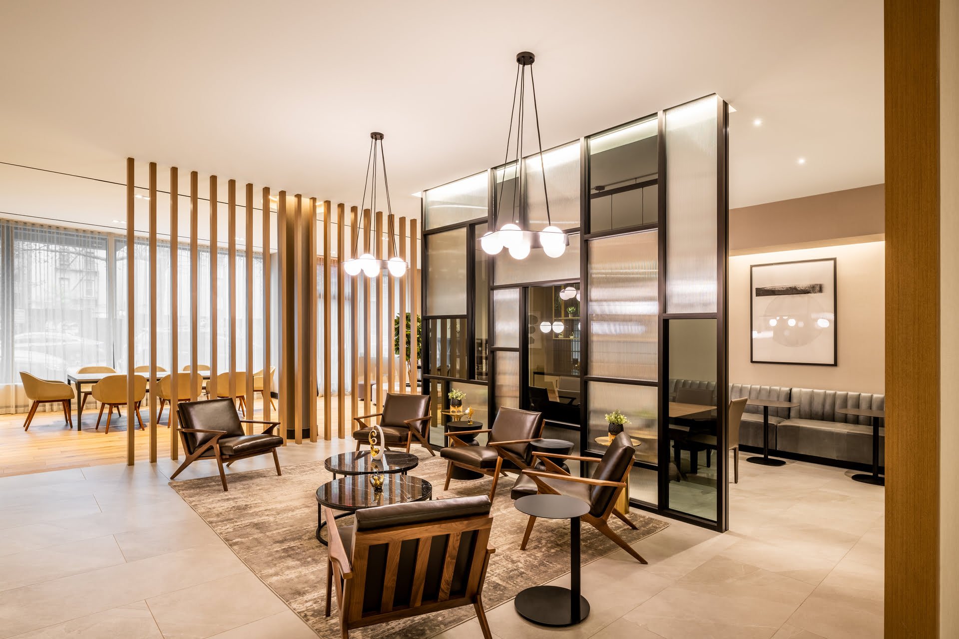Modern hotel lobby with seating area, wooden panel decor, black leather chairs, glass tables, and framed black and white artwork.