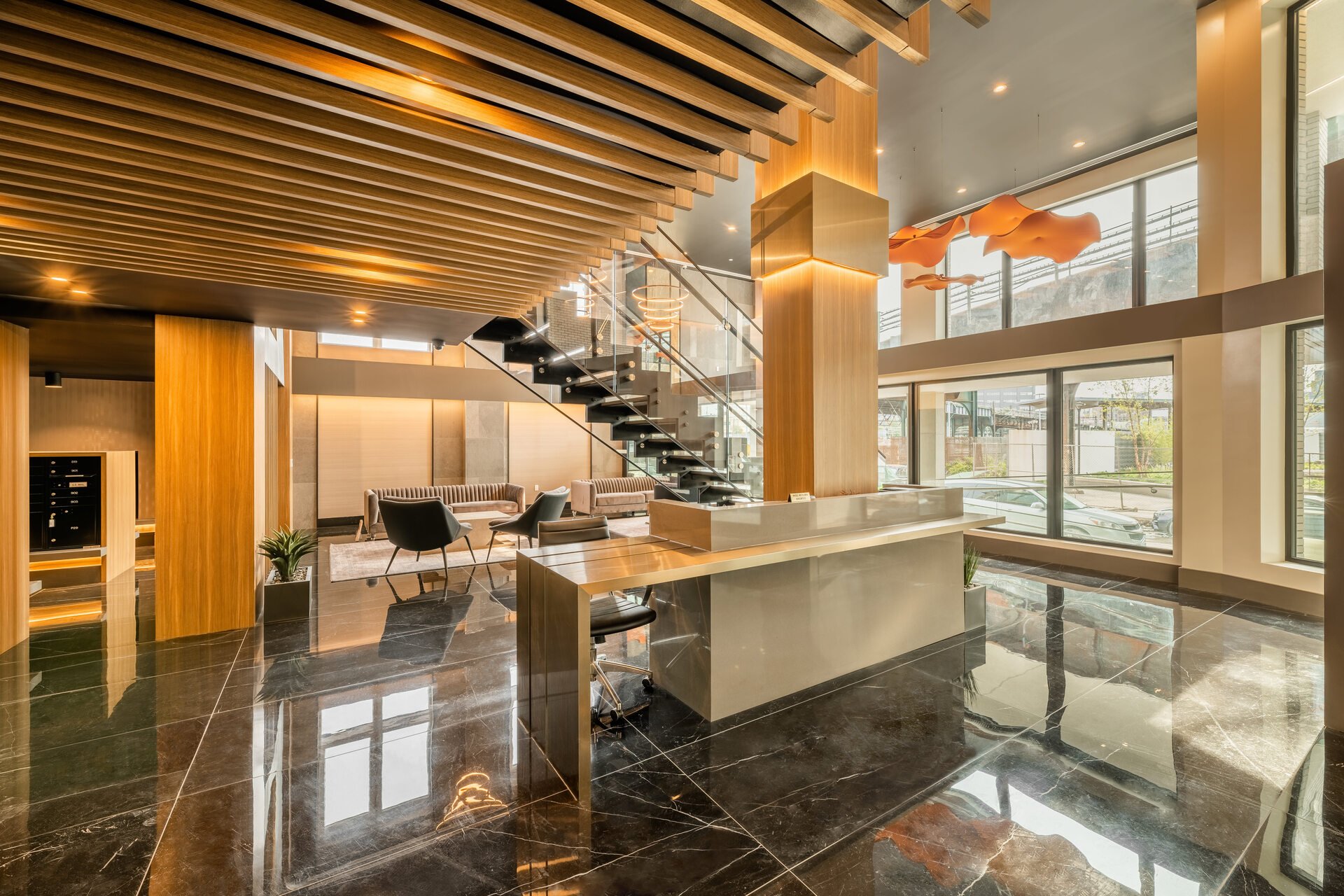 Modern lobby with wooden ceiling accents, glass staircase, and large windows letting in natural light.