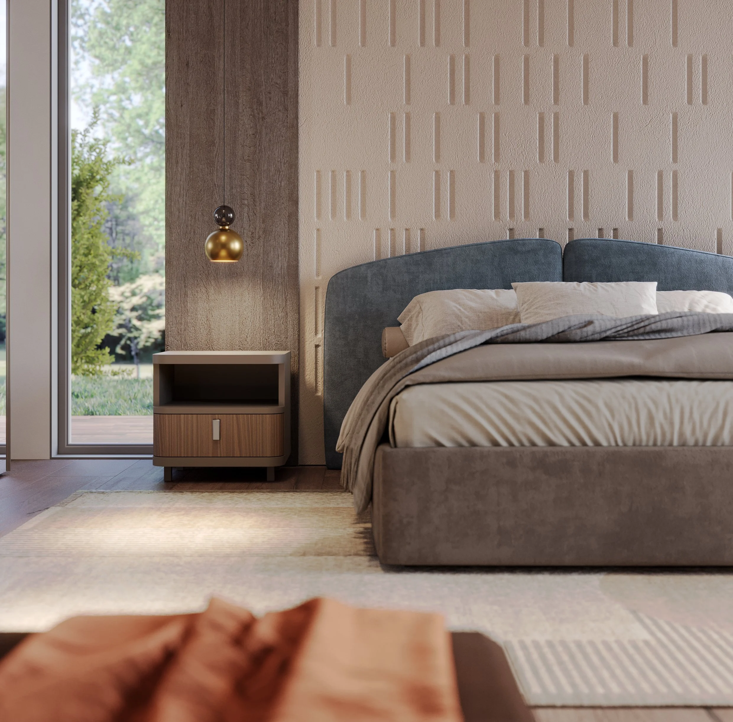 View of a bedroom with a blue upholstered bed, beige and gray bedding, wooden nightstand, and a textured beige wall with vertical indentation patterns. A pendant light with a black and gold spherical design hangs beside the bed. A large window shows green trees outside.