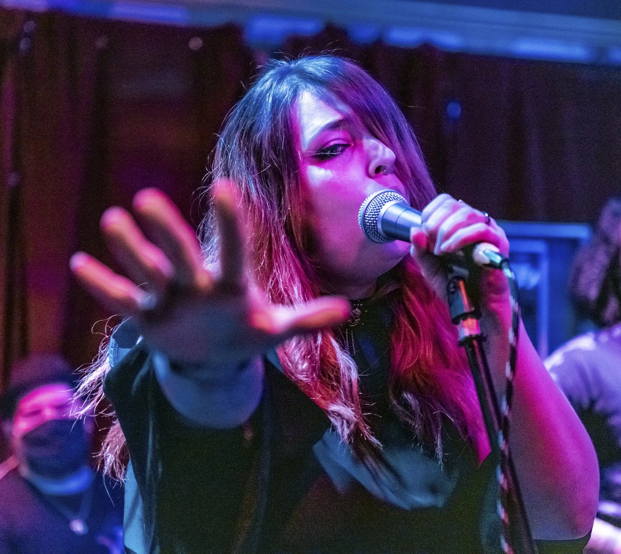 A woman singing into a microphone holding her hand out reaching for the camera