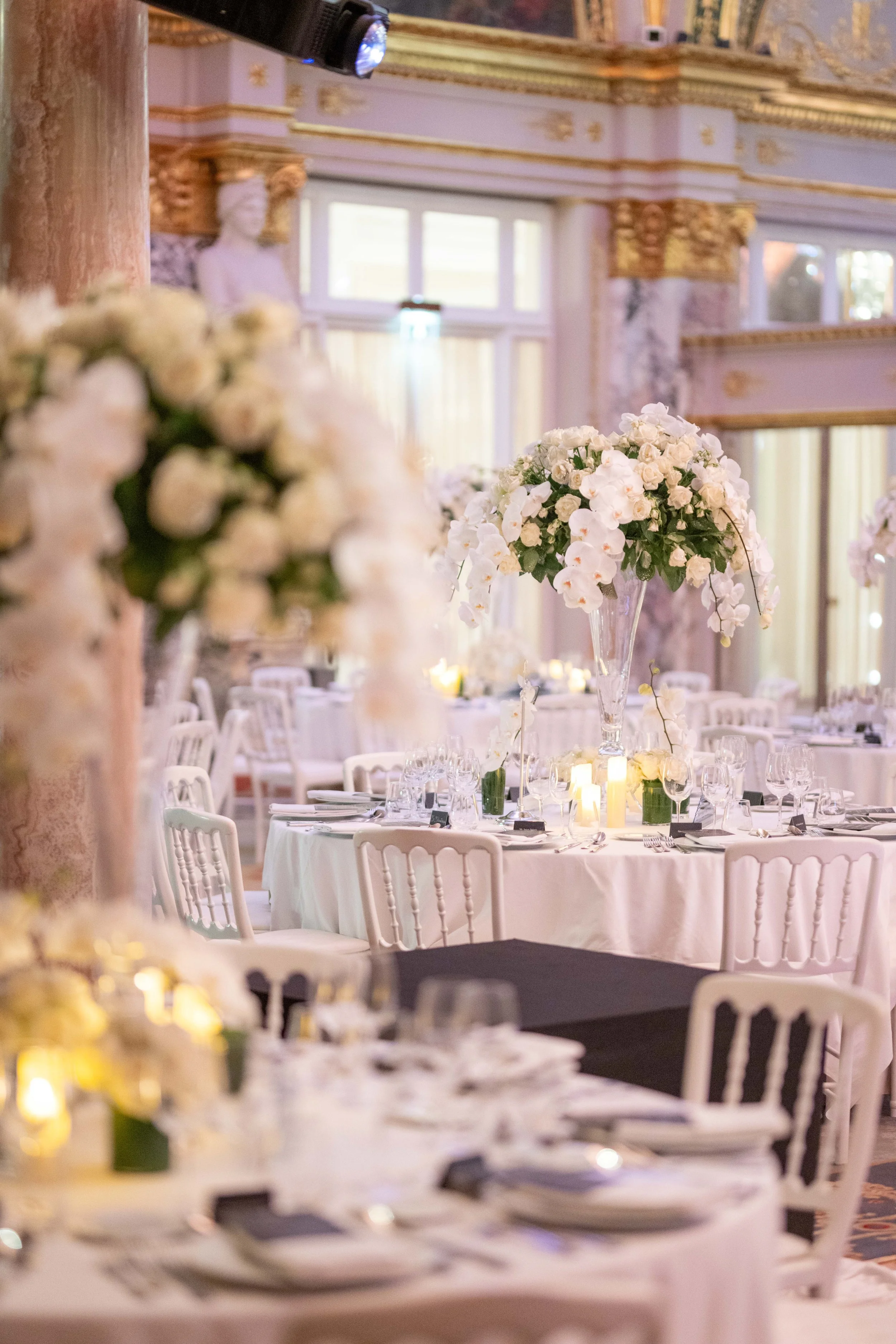 Salle de réception décorée avec des vases de fleurs blanches et des bougies, en vue d'un événement ou d'une célébration.