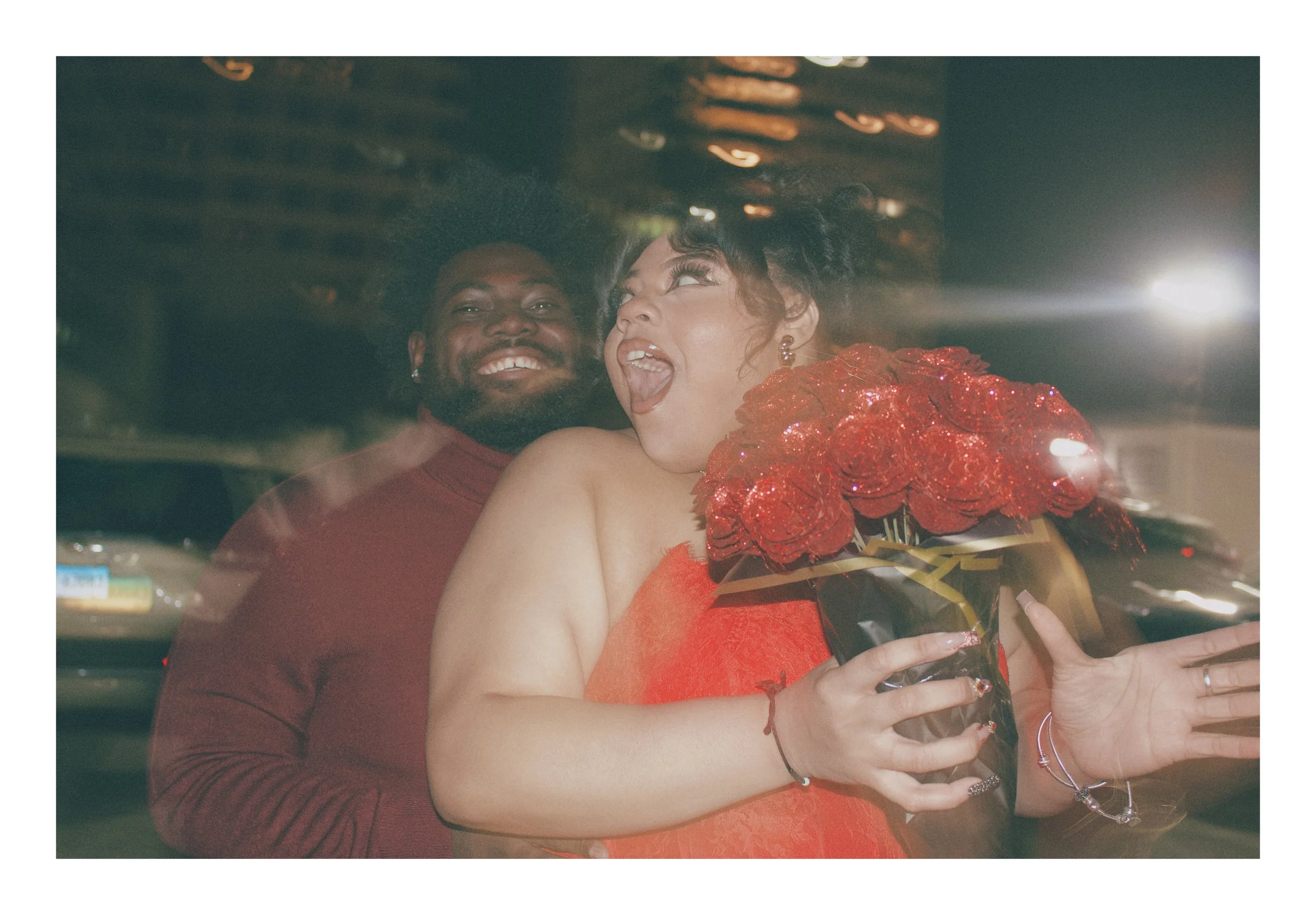 Excited woman holding a large bouquet of red roses next to her smiling partner during a nighttime anniversary session in Avon.