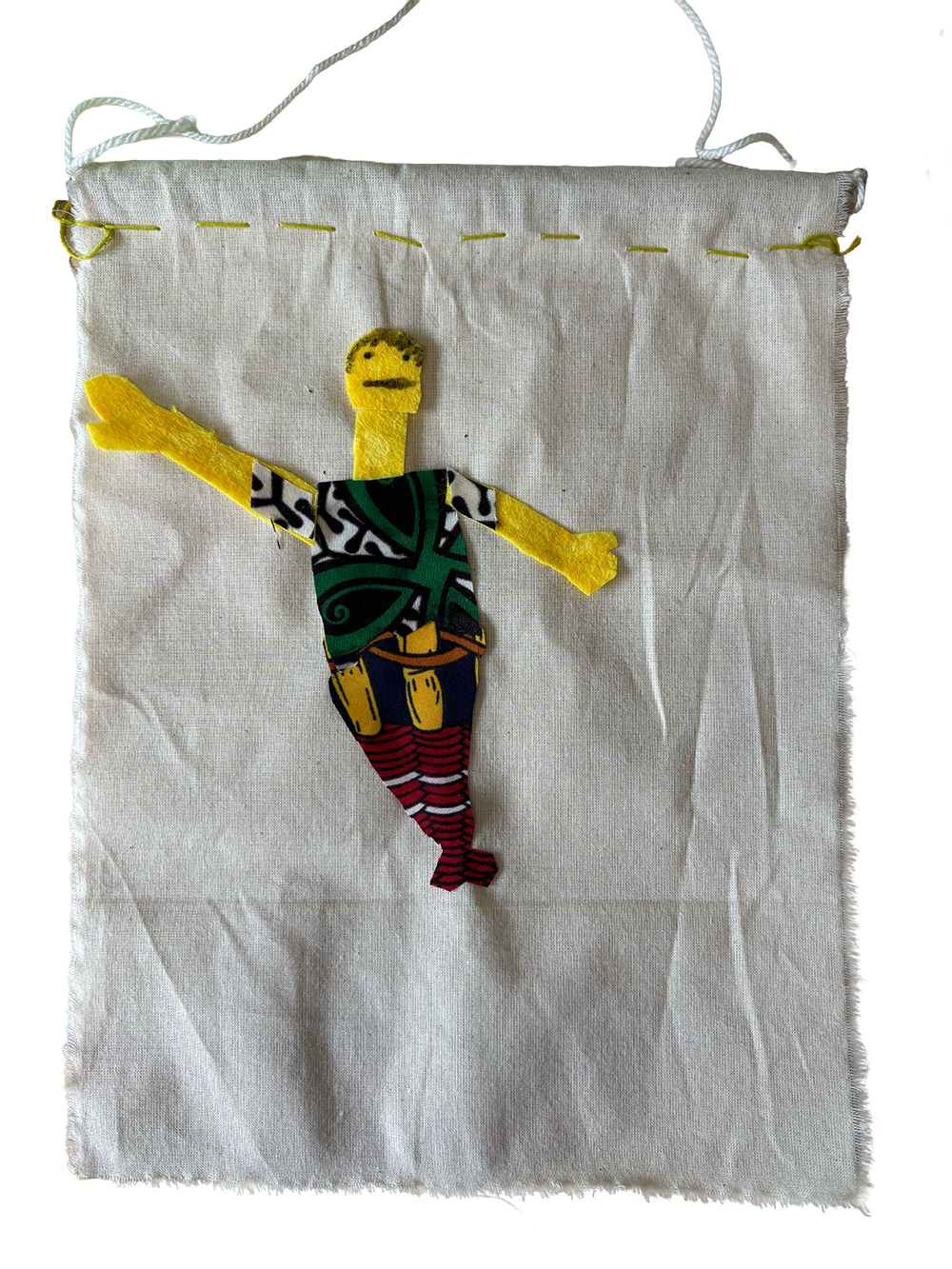 A fabric puppet resembling a person, made with colorful felt pieces, with yellow arms, a patterned green torso, striped red pants, and a yellow head with simple face details, attached to a white cloth background.