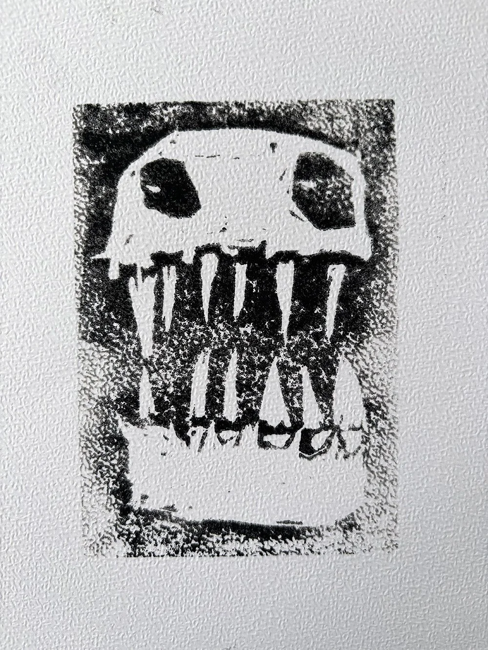 A black and white lino print of a monster with a dripping mouth on a wall.