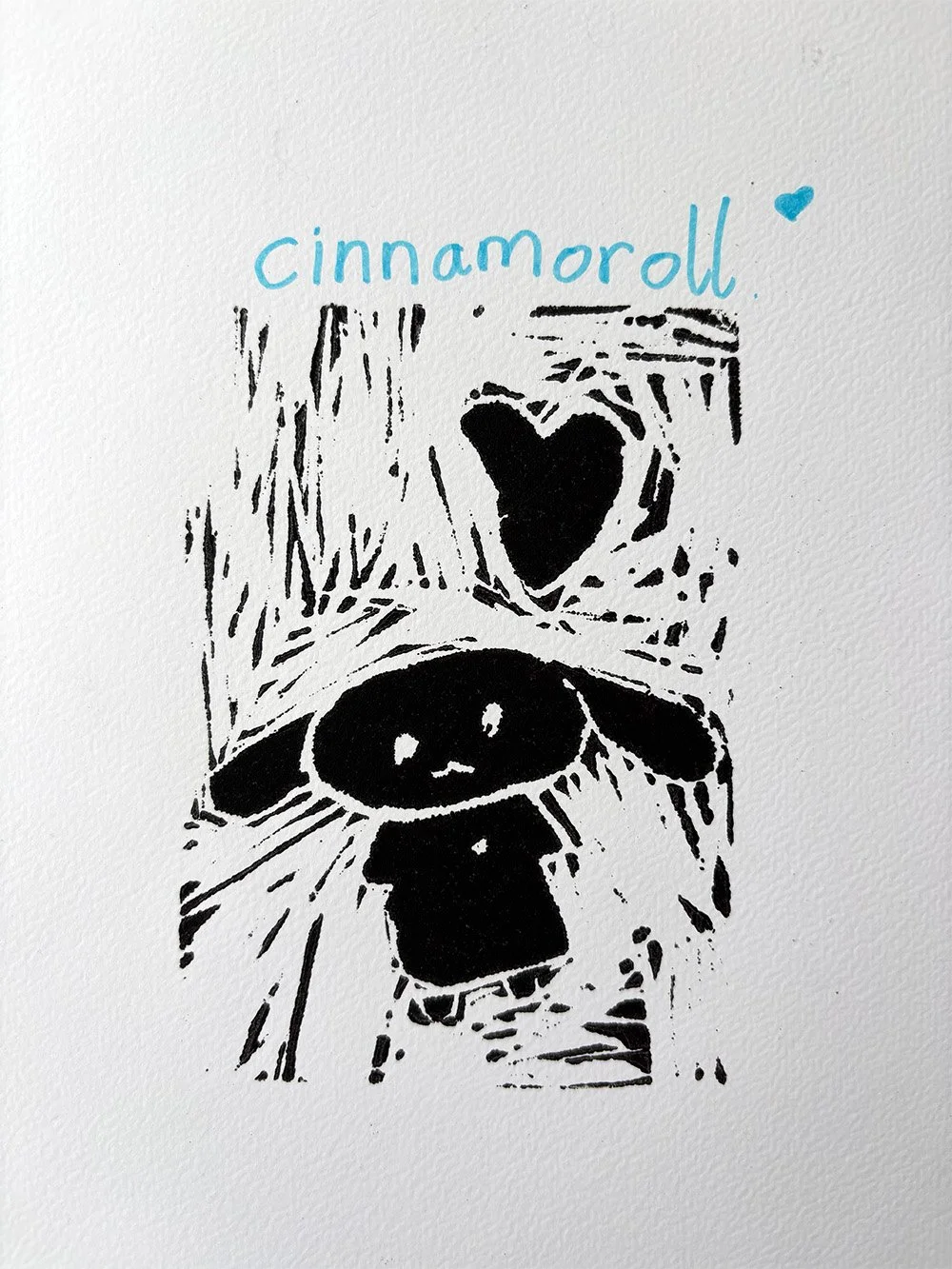 A black and white lino print of a small creature with a round head and big eyes, holding a heart-shaped object, underneath the word "cinnamoroll" written in light blue with a small blue heart.
