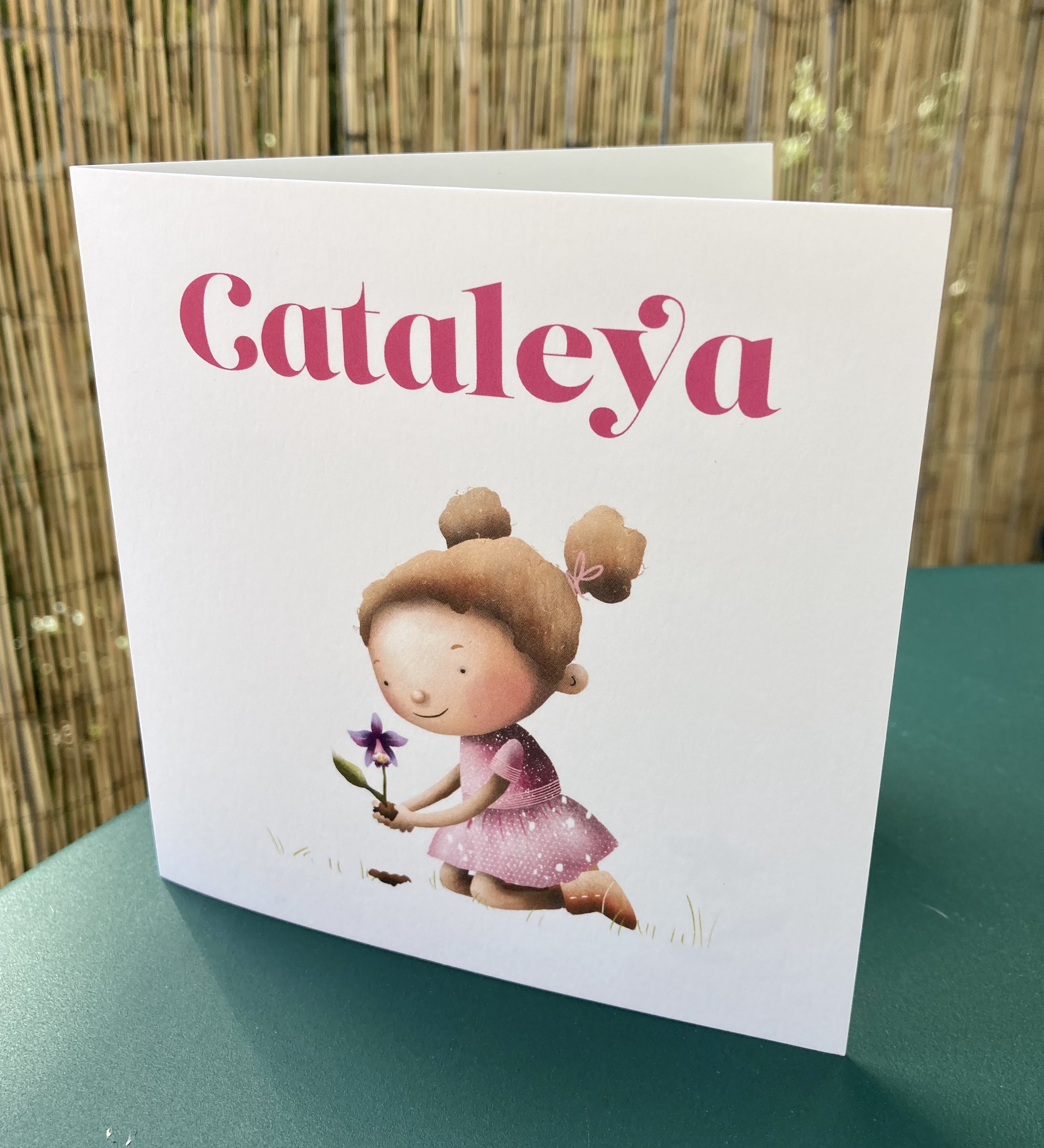 A greeting card with a cartoon girl holding a purple flower, wearing a pink polka dot dress and a crown of brown hair.