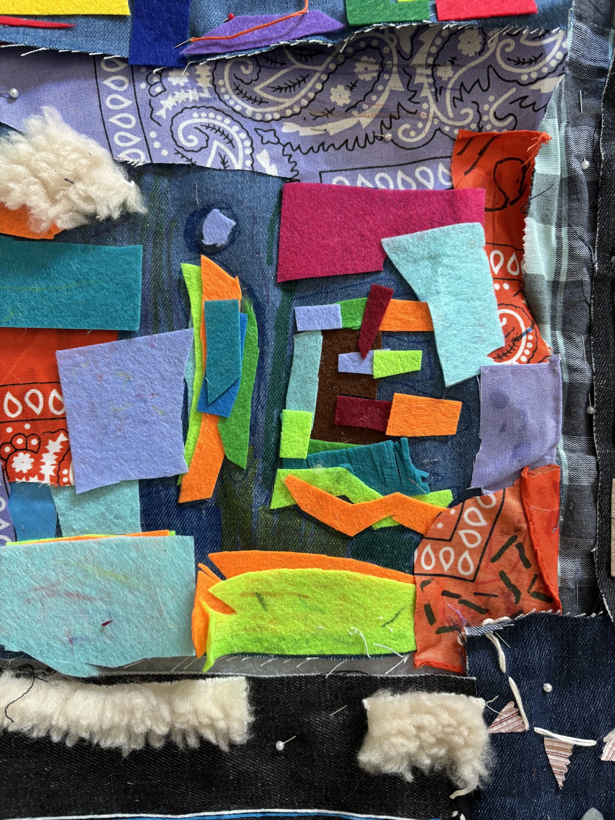 A mixed media quilt with fabric and felt pieces in bright colors, including red, purple, pink, blue, green, teal, orange, and white, sewn onto a dark background with some cotton fluffy patches and pins.