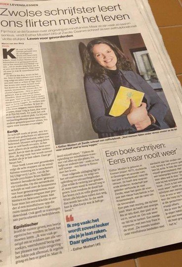Artikel in een krant met een foto van een jonge vrouw die een boek vasthoudt en glimlacht.