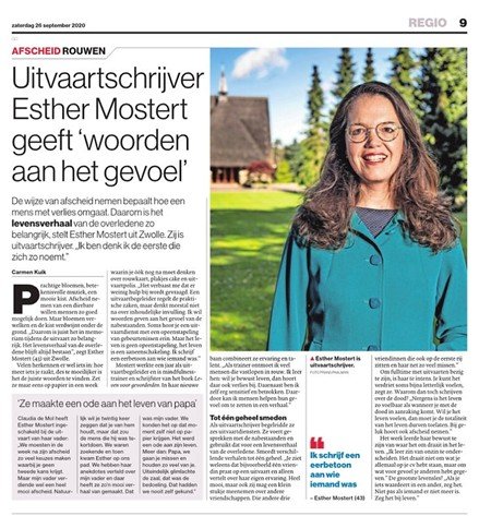 Foto van Esther Mostert die lacht, met een blauwe jas, in een tuin met groen bomen en een huis op de achtergrond.