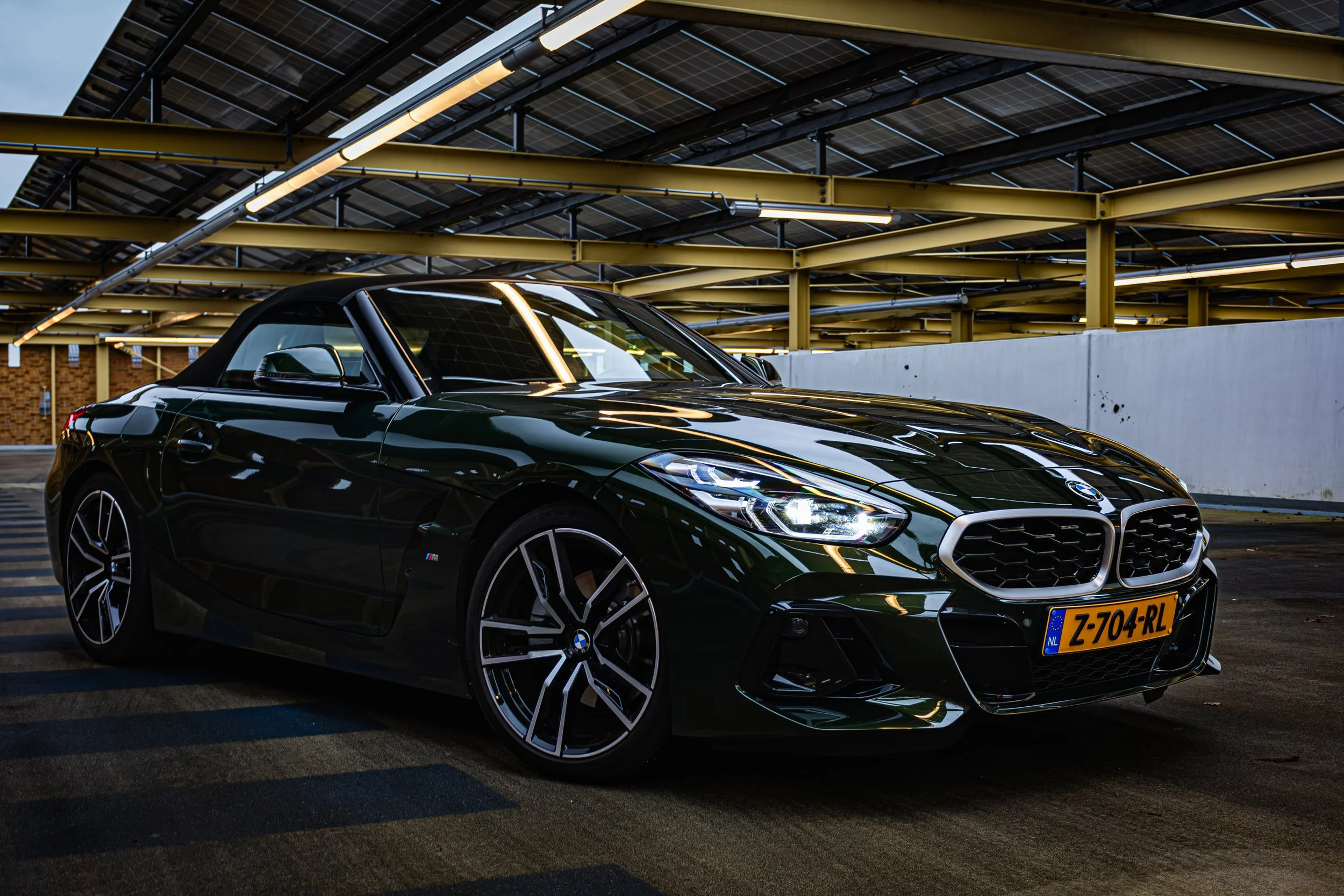 Een zwarte BMW cabrioletauto geparkeerd onder een parkeergarage met zonnepanelen en gele metalen structuren.