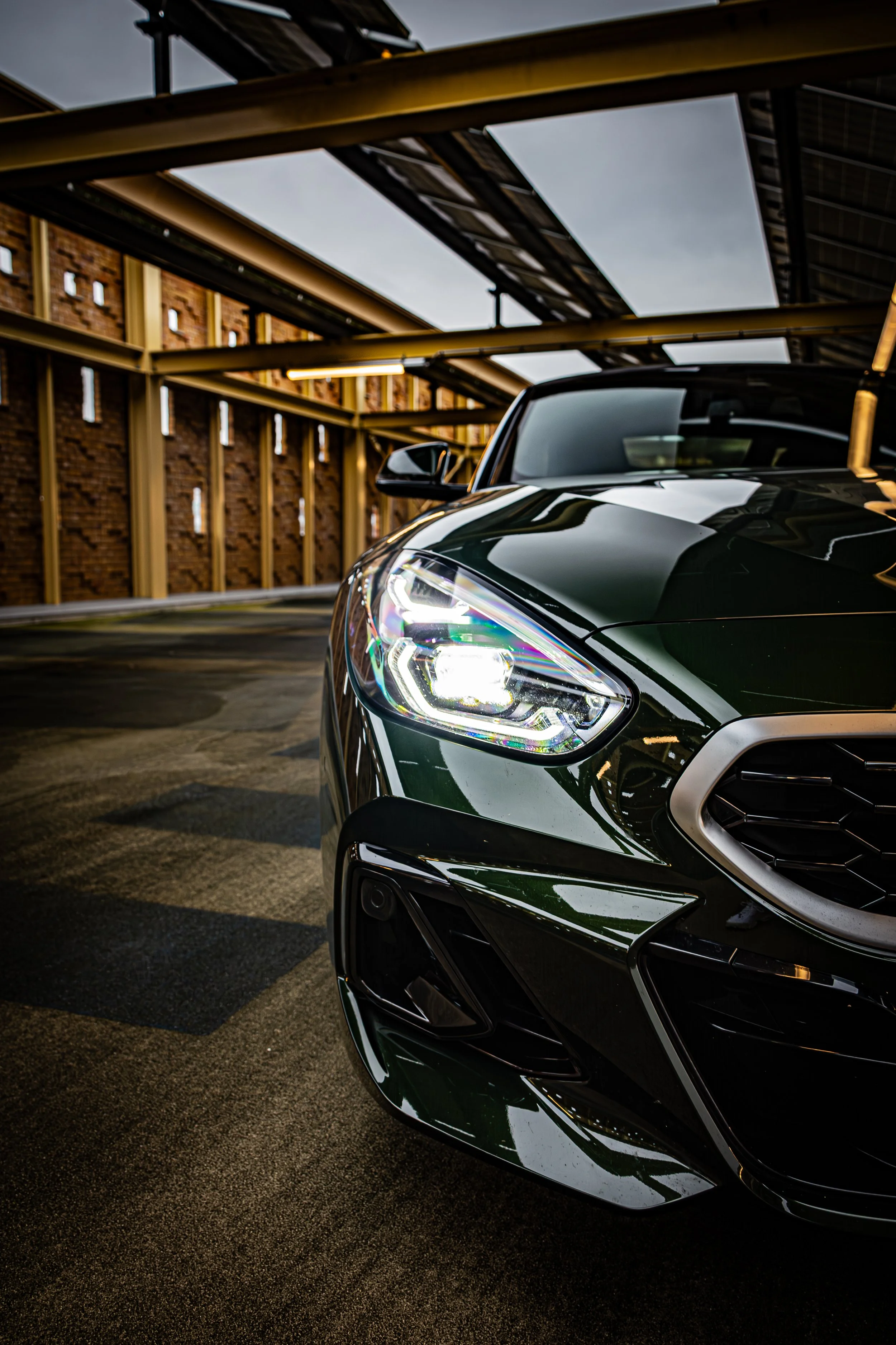 Een close-up van de voorzijde van een zwarte moderne auto in een parkeergarage met houten muren, met opvallende koplampen en reflecterend oppervlak.