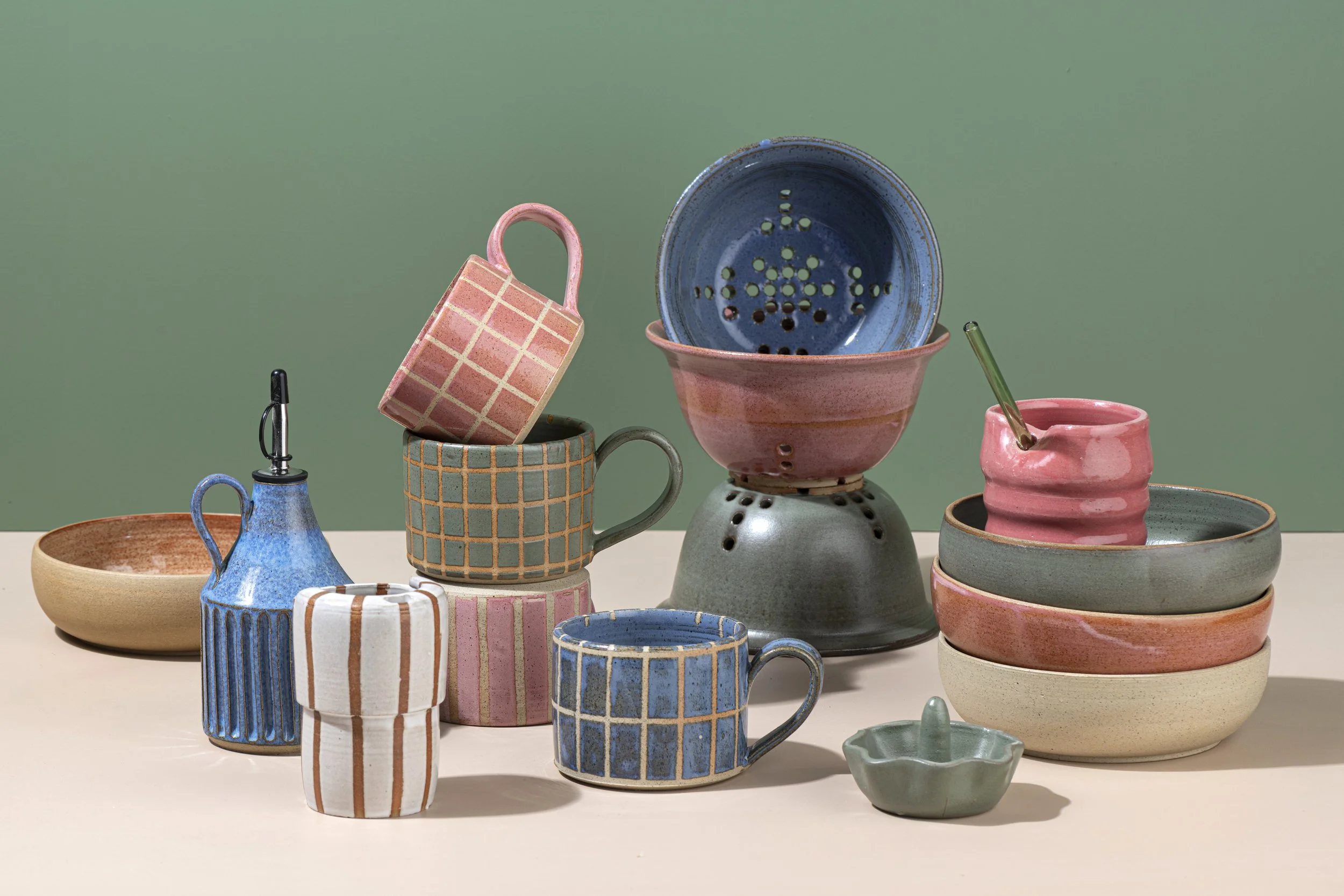 A collection of colorful ceramic dishes and mugs with geometric patterns, arranged on a white surface with a green background.