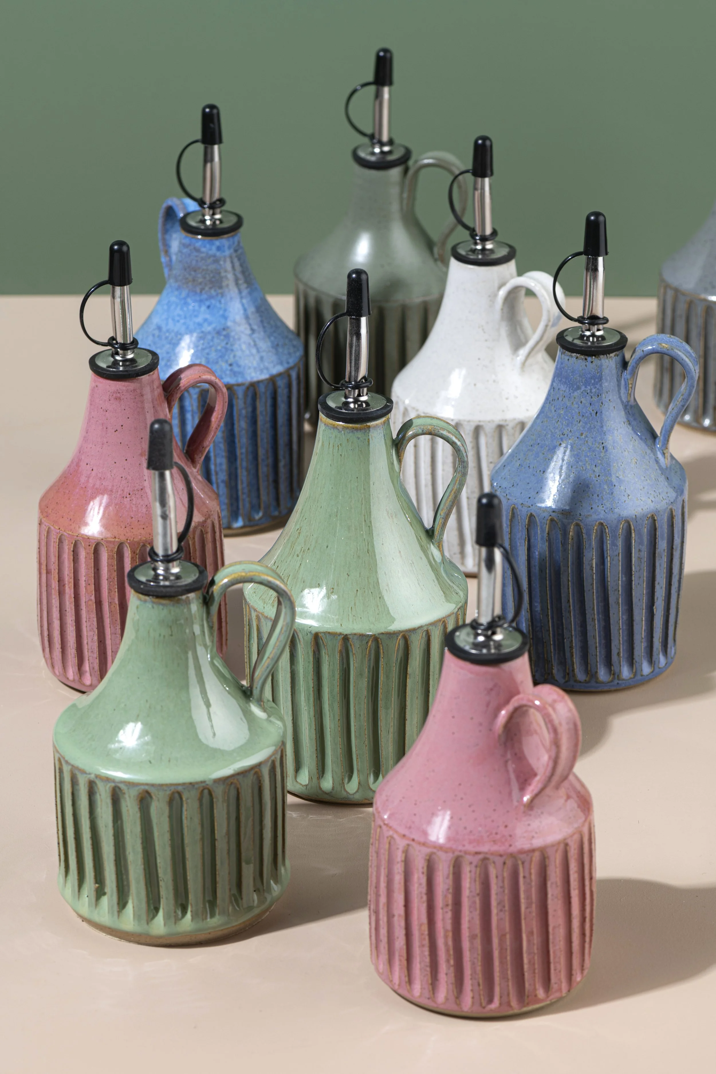 Colorful ceramic oil cruets with stoppers on a beige surface, against a green background.