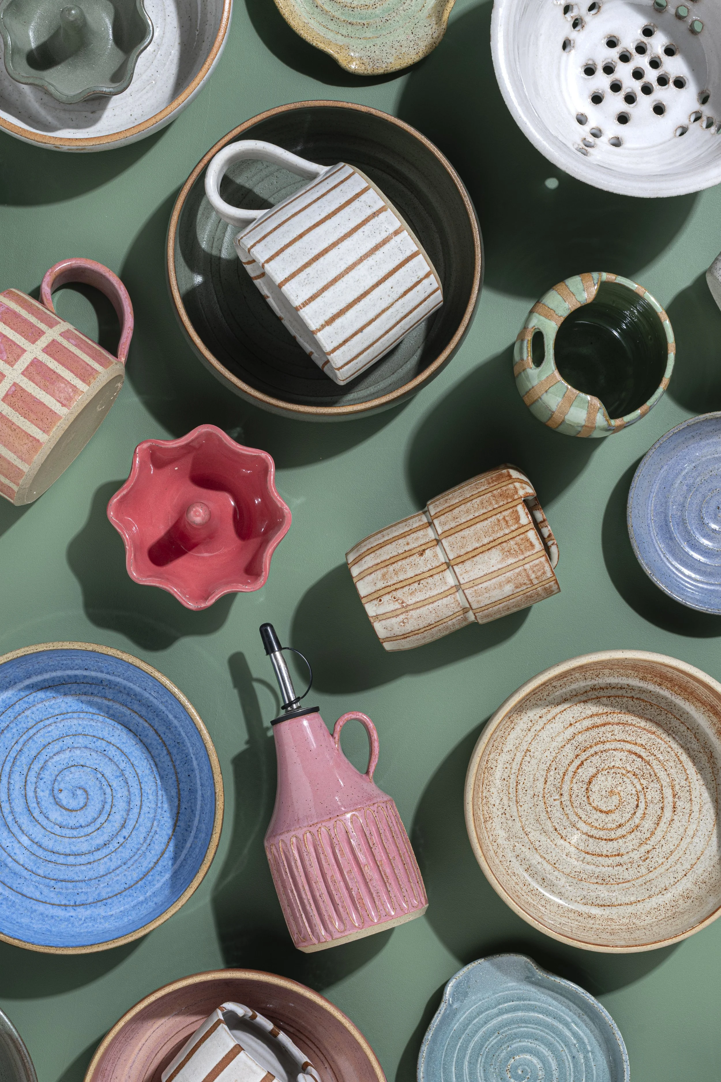 A collection of various ceramic bowls and mugs with striped and dotted patterns in colors like pink, blue, green, white, and brown, arranged on a green surface.