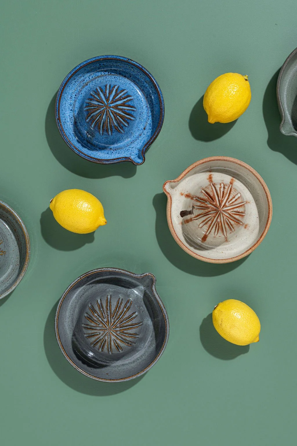 Multiple ceramic bowls with a starburst pattern, and three lemons on a green surface.