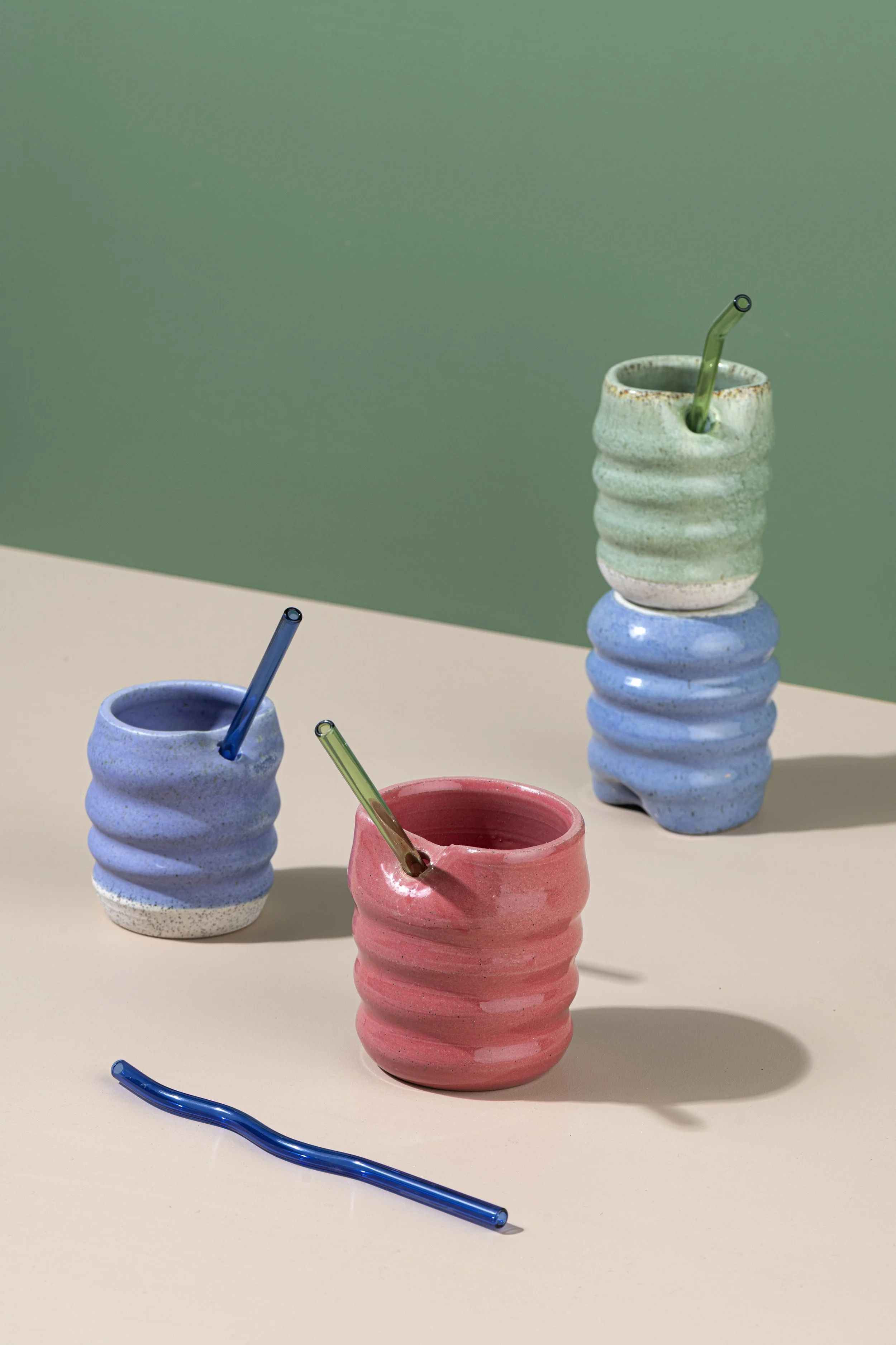 Colorful ceramic cups with bendy straws on a beige and green background.