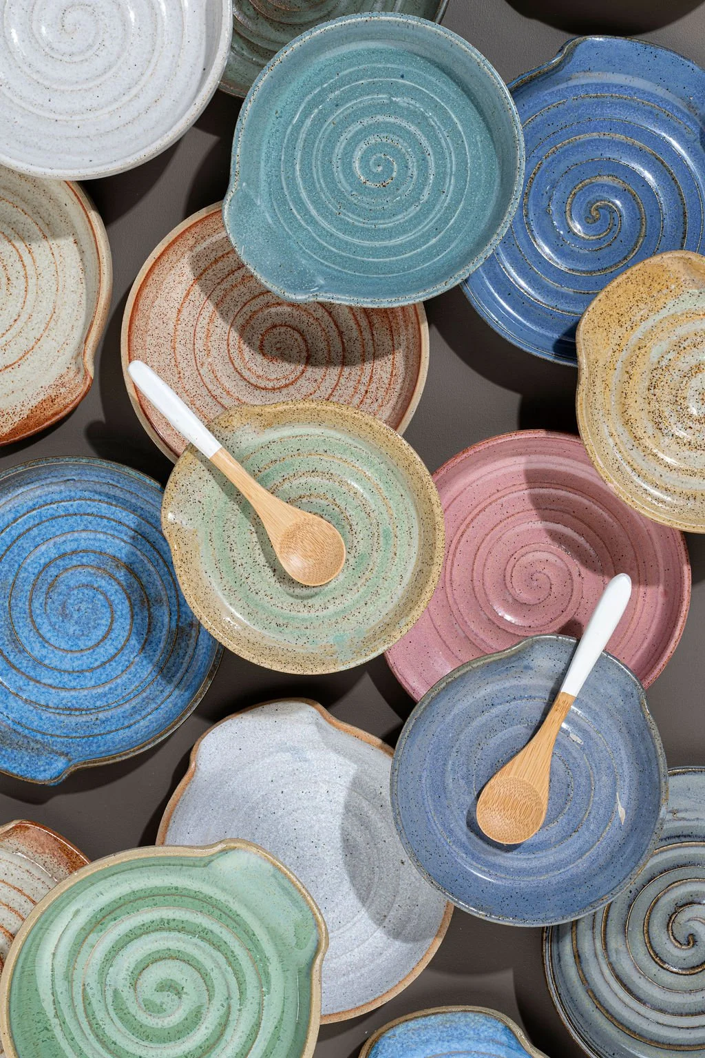 Collection of colorful ceramic spoon rests with spiral patterns and wooden utensils.