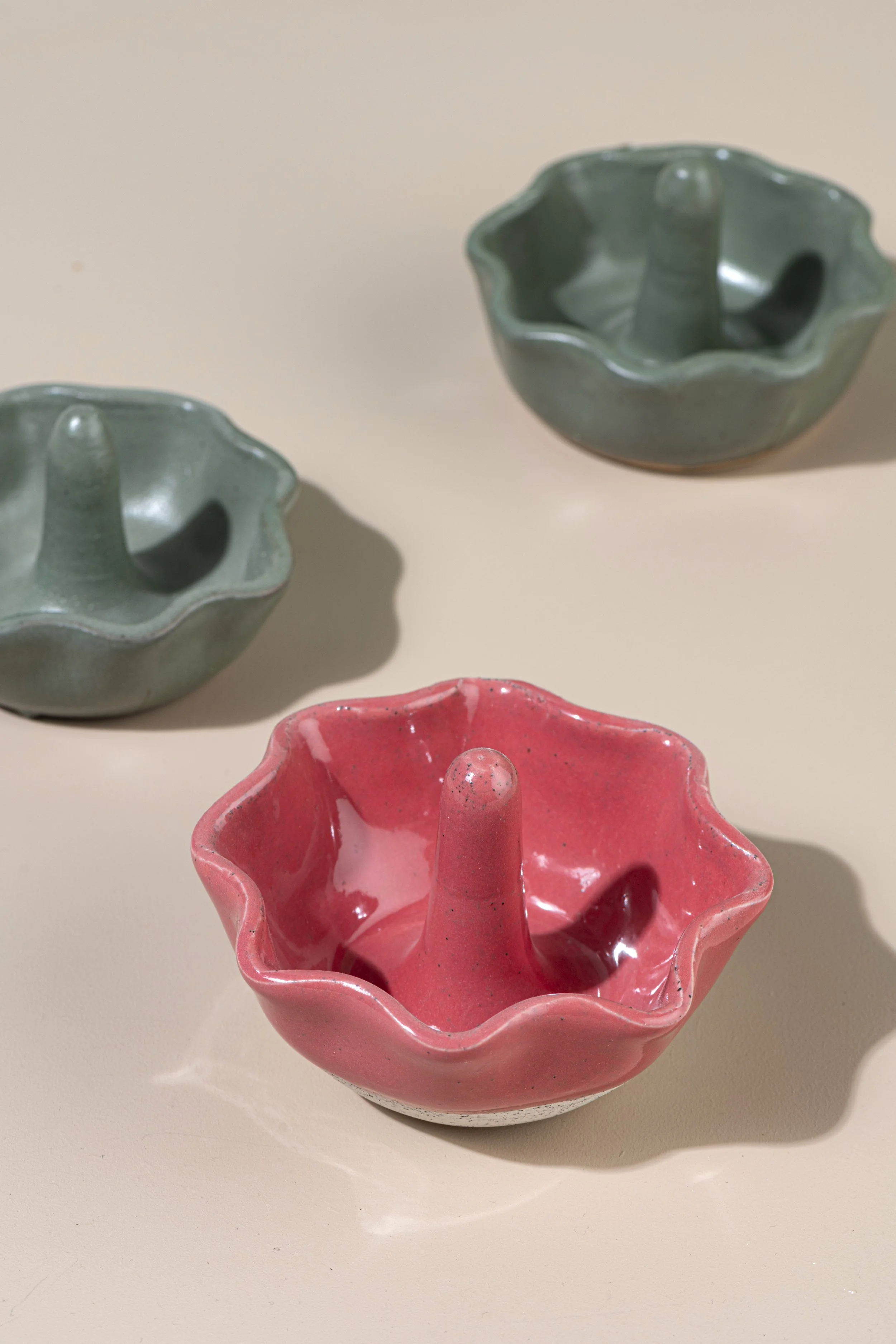 Three flower-shaped ceramic ring trees, two are green and one is pink, placed on a beige surface.