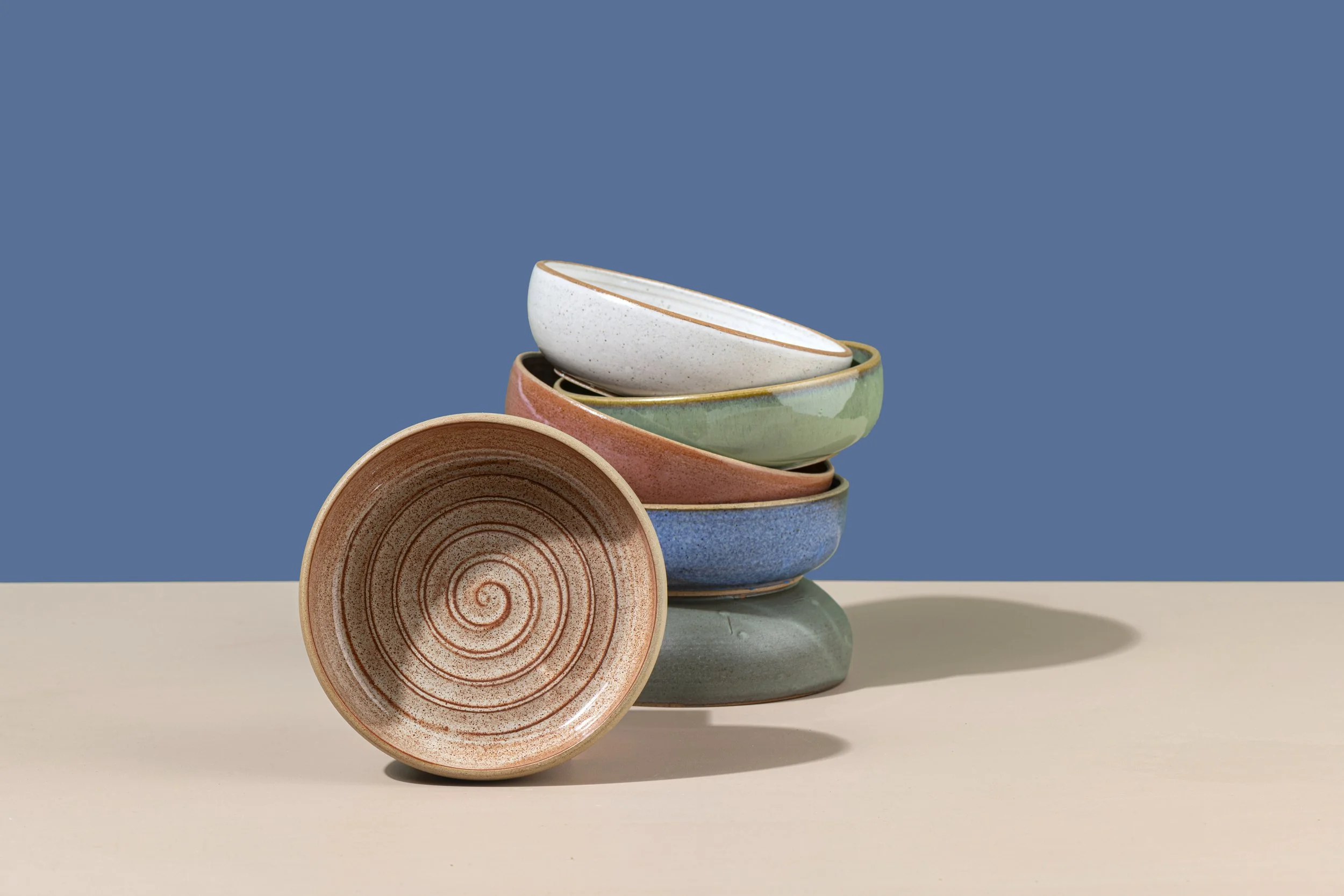 Stacked colorful ceramic bowls on a beige surface with a blue background.