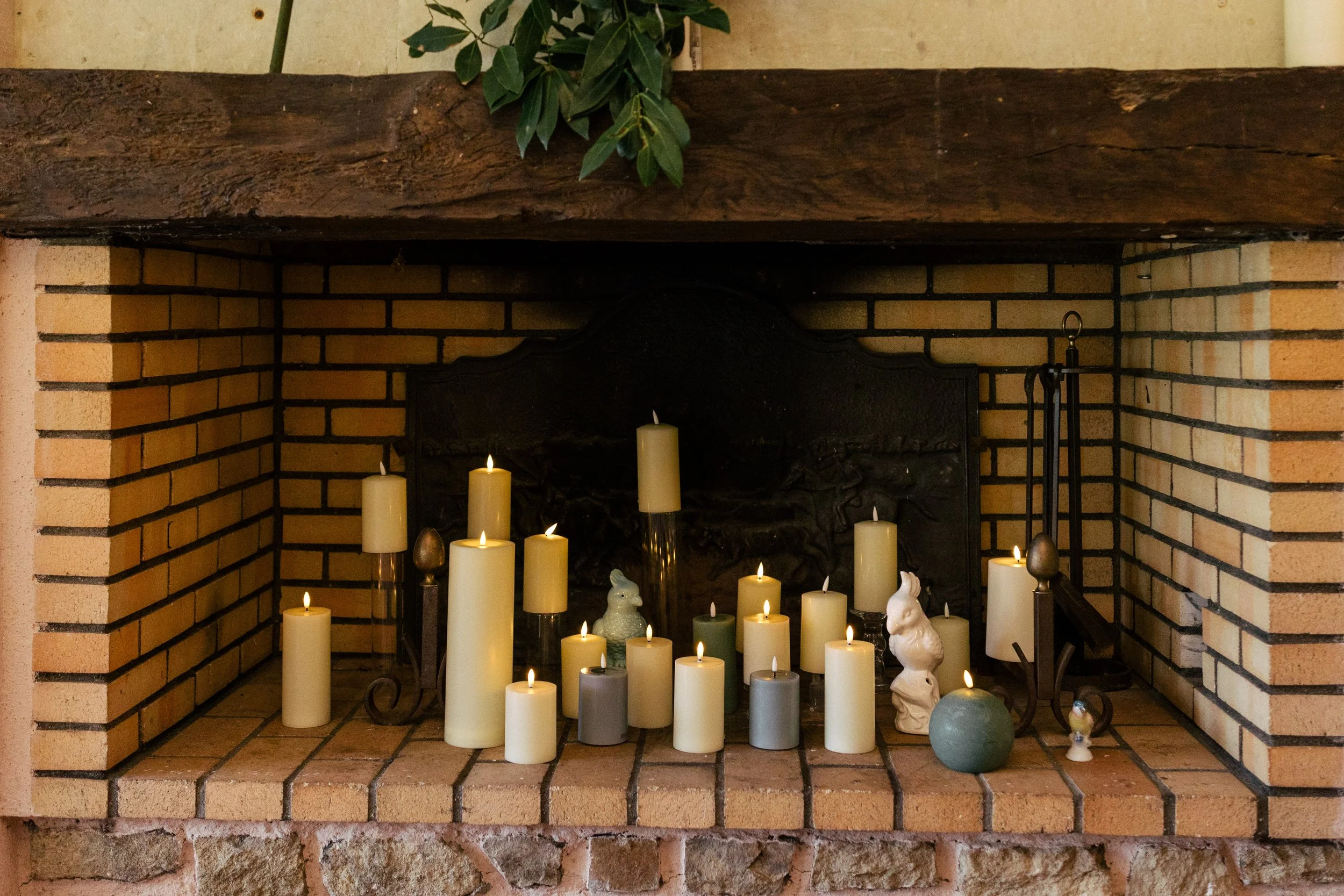 Cheminée en briques avec de nombreuses bougies allumées et quelques décorations en céramique, sur une couchette en bois.