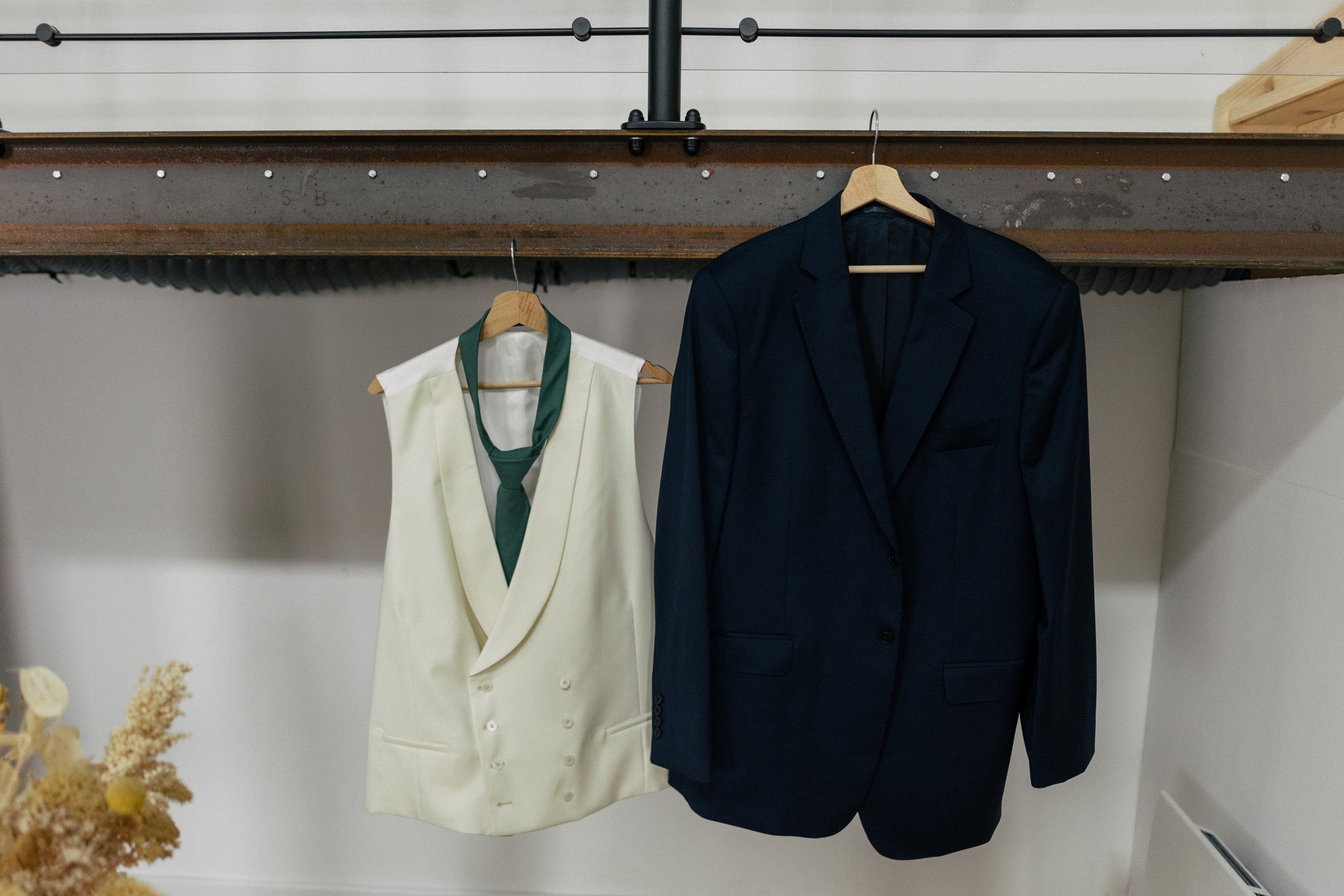 Deux vestes, une blanche avec une cravate verte et une noire, suspendues sur des cintres, dans un placard.
Voici la future tenue du marié qui attend de s'habiller avec son costume trois pièce avant la cérémonie