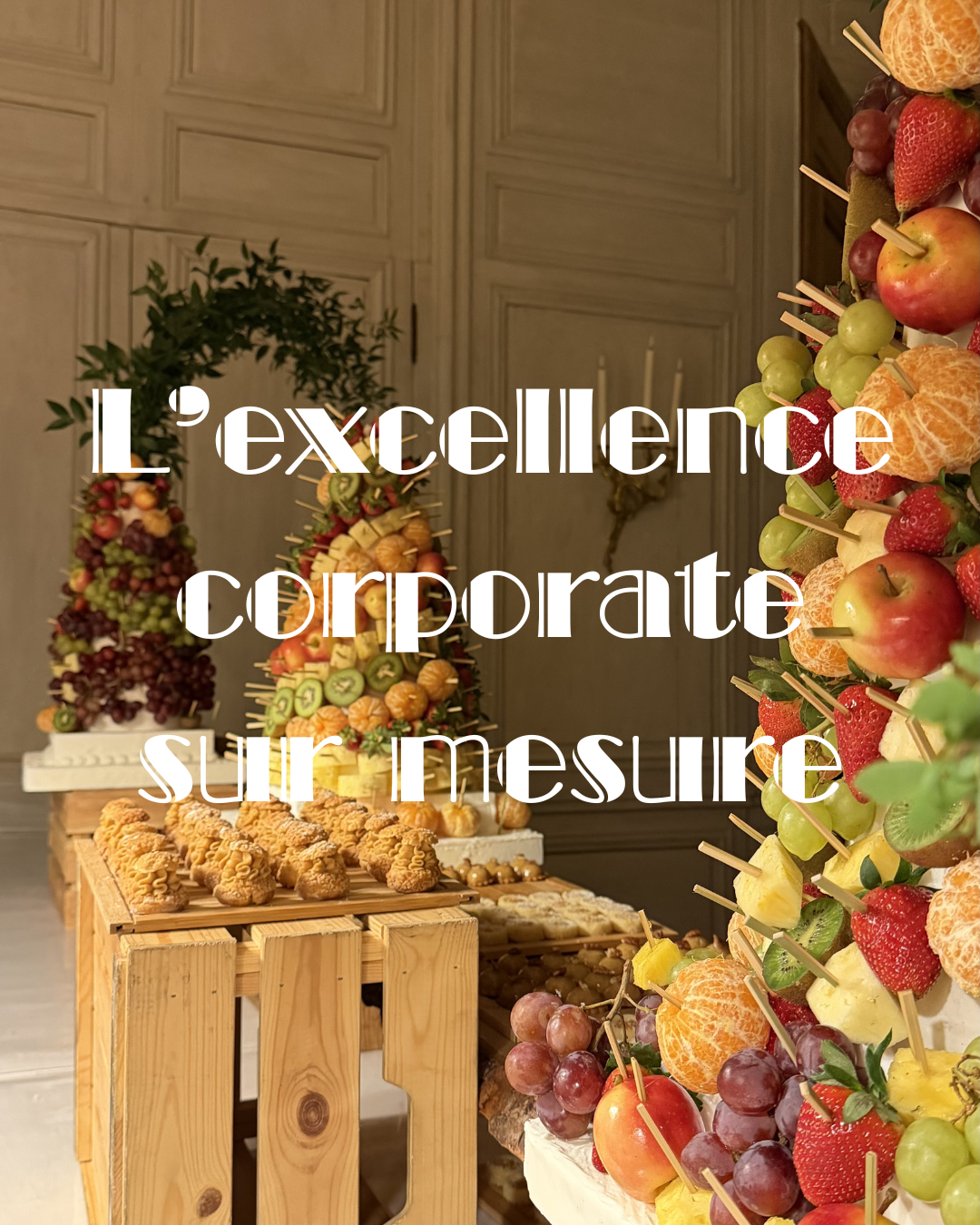 Une table avec des buffets de pyramide de fruits et pâtisseries devant un mur en bois, décoration de fruits sur brochettes et choix de desserts variés.