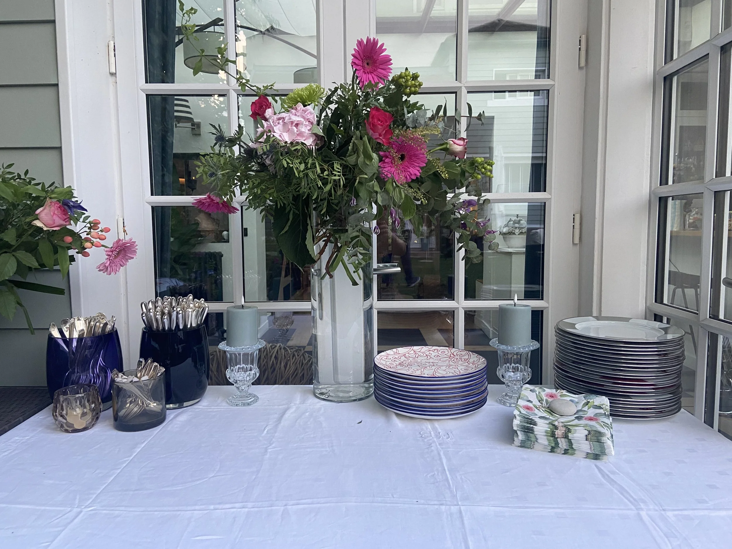 Une table dressée avec des assiettes, des verres et des serviettes, devant un grand bouquet de fleurs colorées sur une fenêtre en arrière-plan, lors de fiançailles