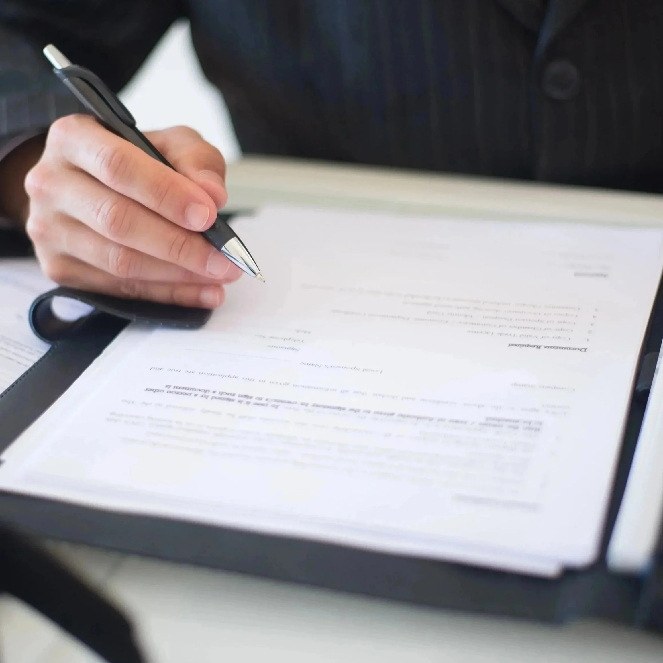 Close-up of a person’s hand holding a black pen and writing on a document with printed text.