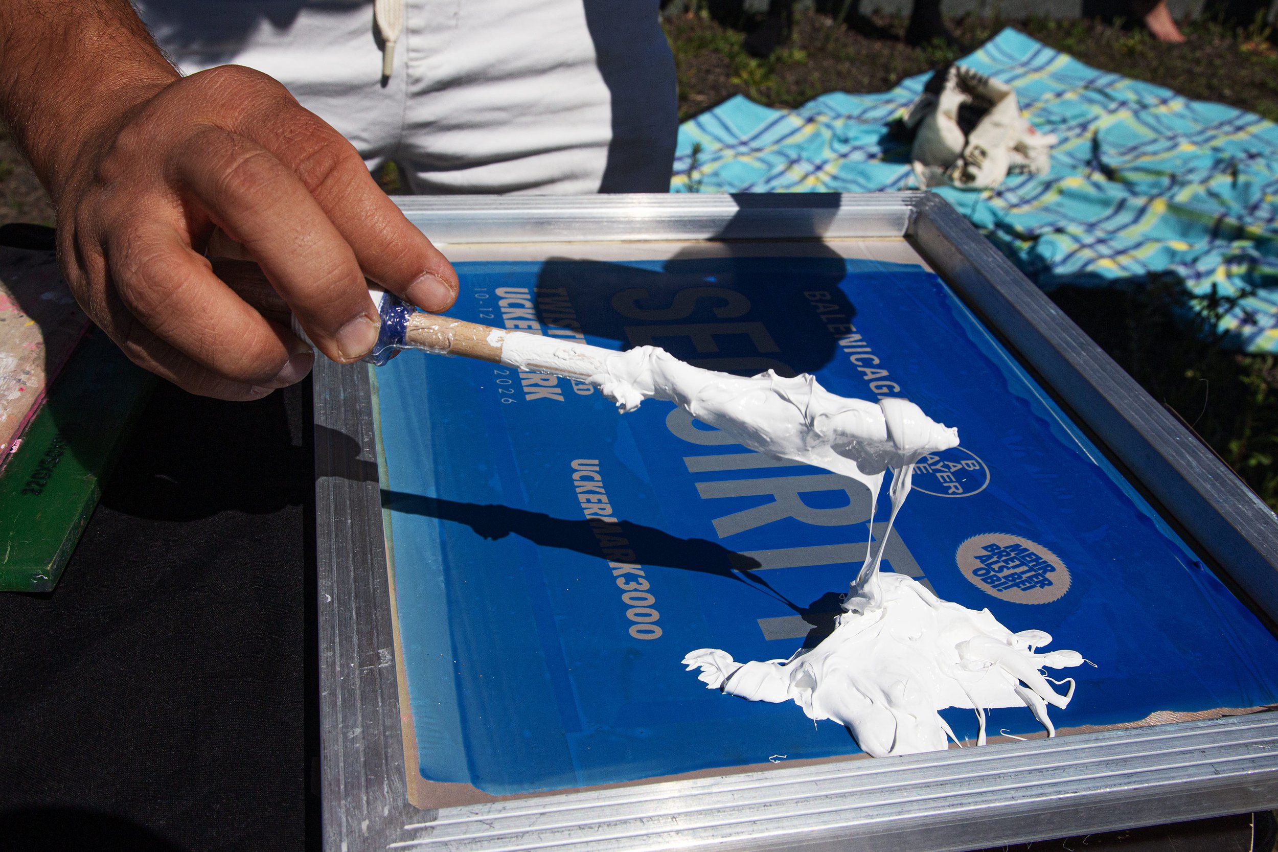 A person spreading white screenprint ink on a silkscreen. The silkscreen actions is about to started.