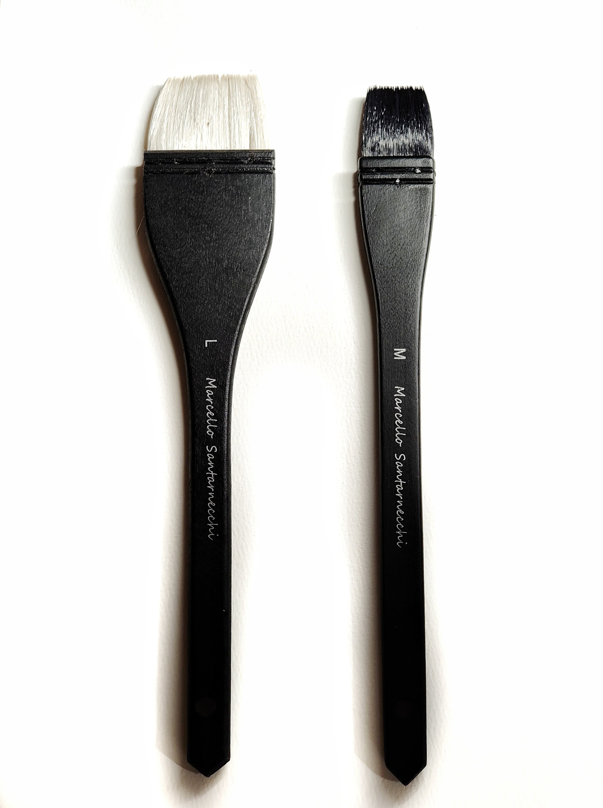 Deux pinceaux de maquillage avec des poils blancs et noirs, placés côte à côte sur un fond blanc.