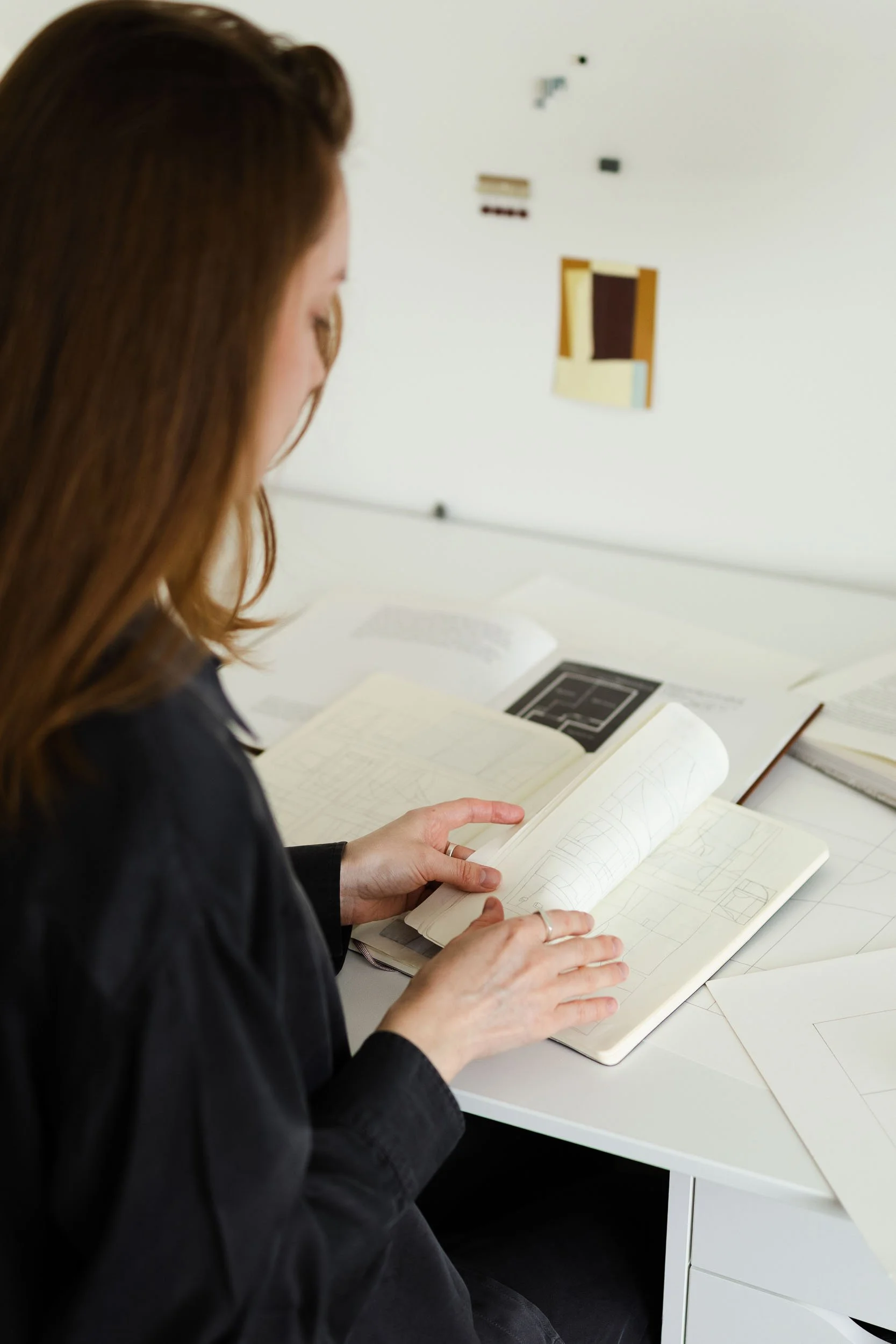 Contemporary visual artist looking through a sketchbook with geometric designs at a studio table with research books.