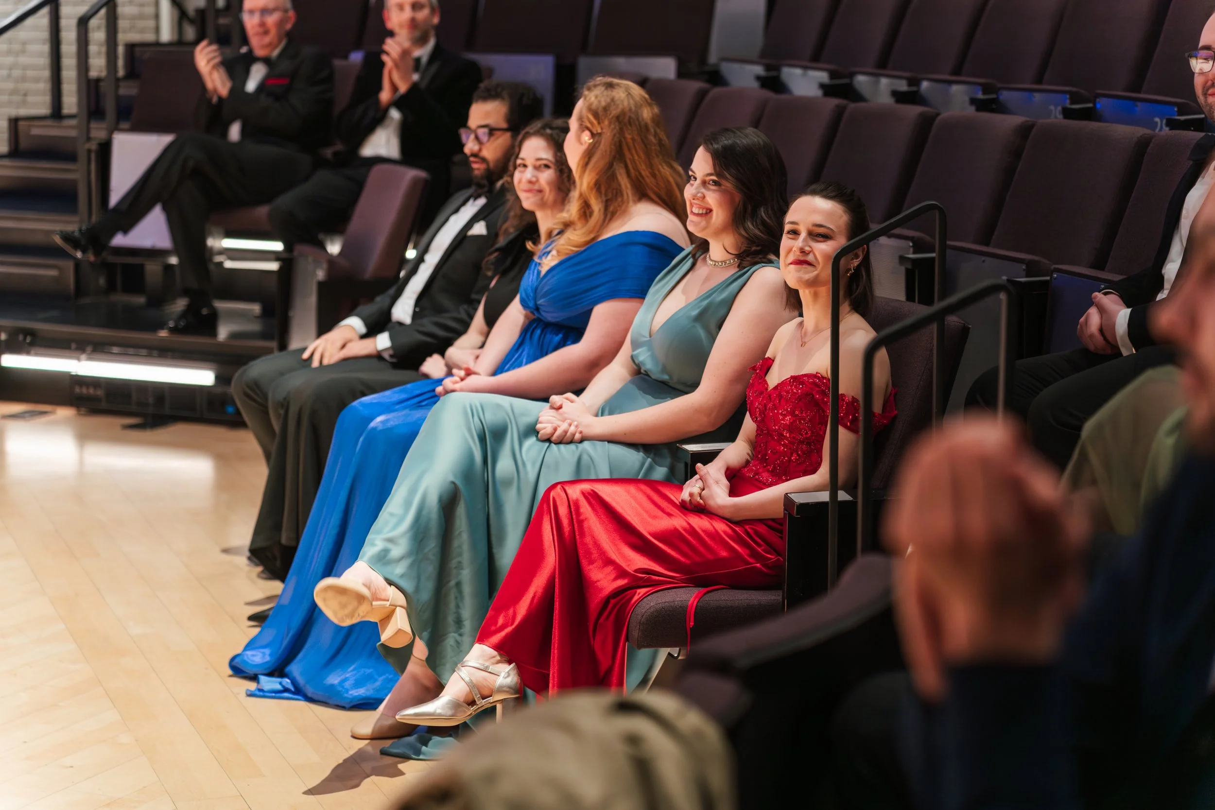 People dressed in formal attire sitting in an auditorium watching a performance or event.