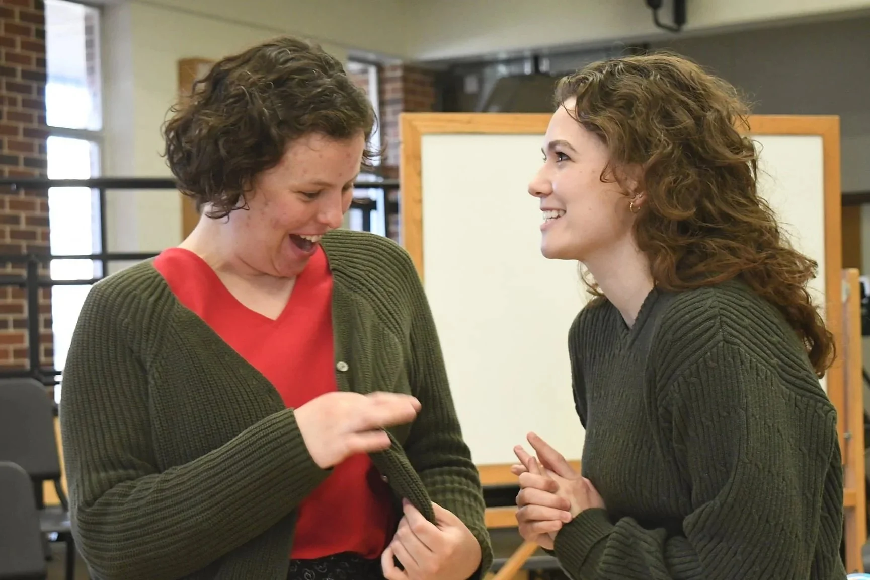 Two women with curly hair smiling and laughing together in an indoor setting.