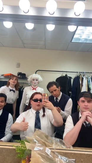 Group of young people dressed in vintage-style school uniforms taking a mirror selfie in a dressing room.