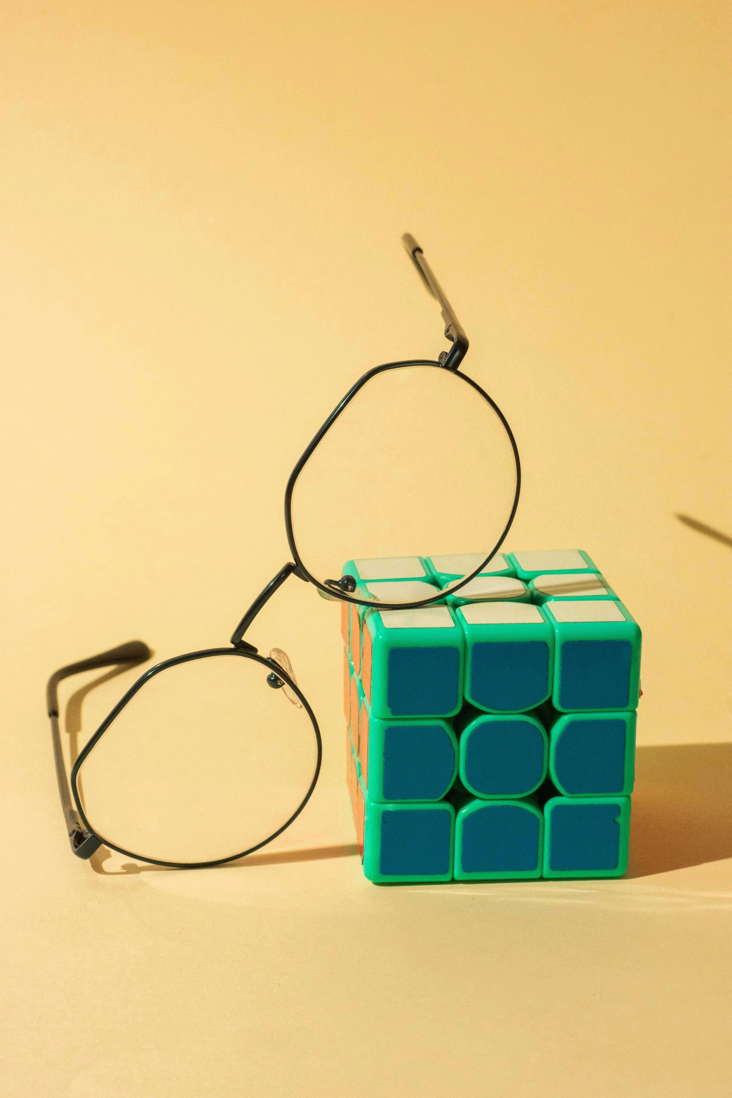 Close-up of a small group of optical illusion magnetic cubes stacked and a pair of glasses resting on the floor. The background feature a plain neutral-colored wall.