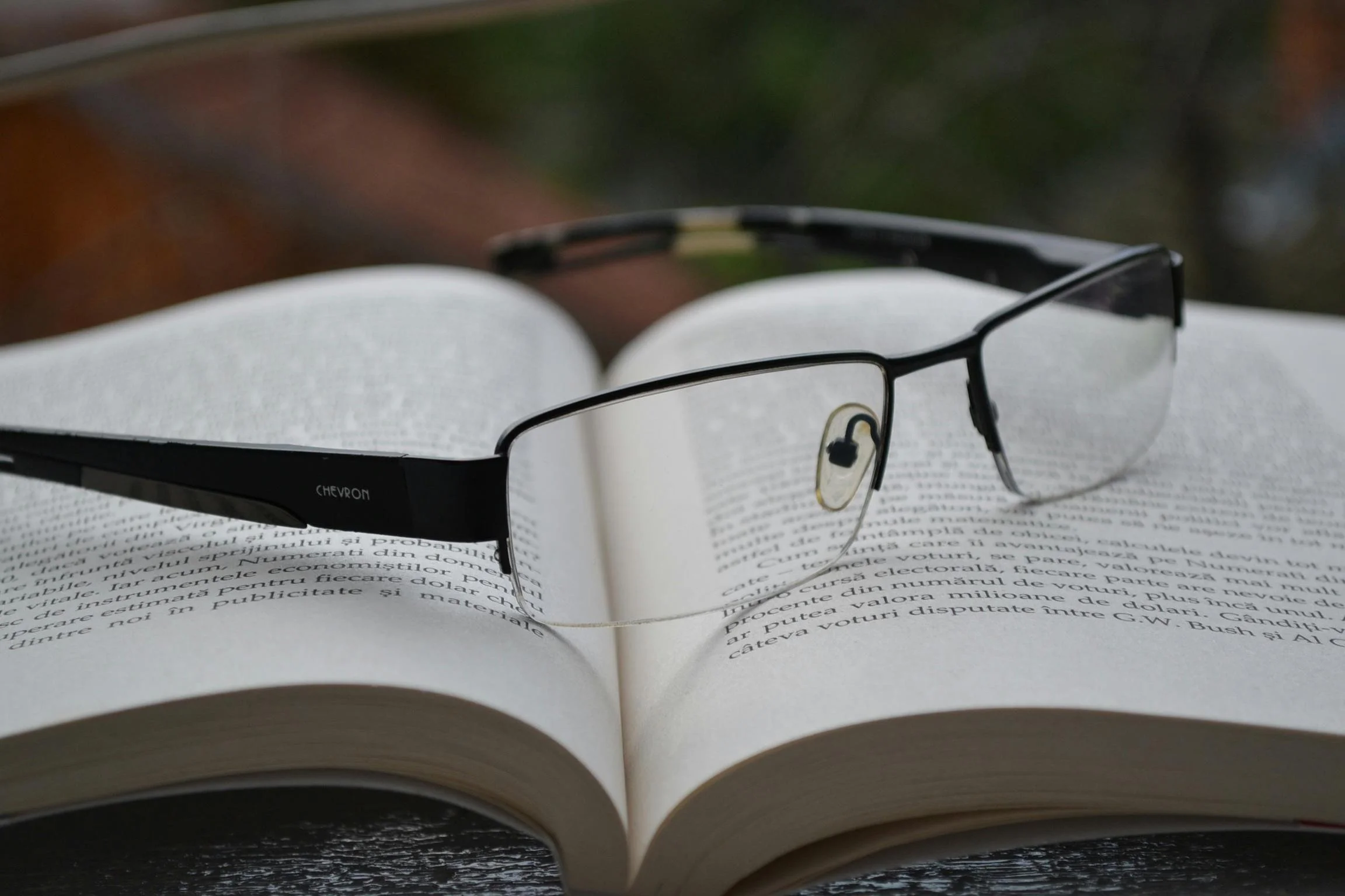 A pair of black-rimmed reading glasses resting on an open book with text in a foreign language.