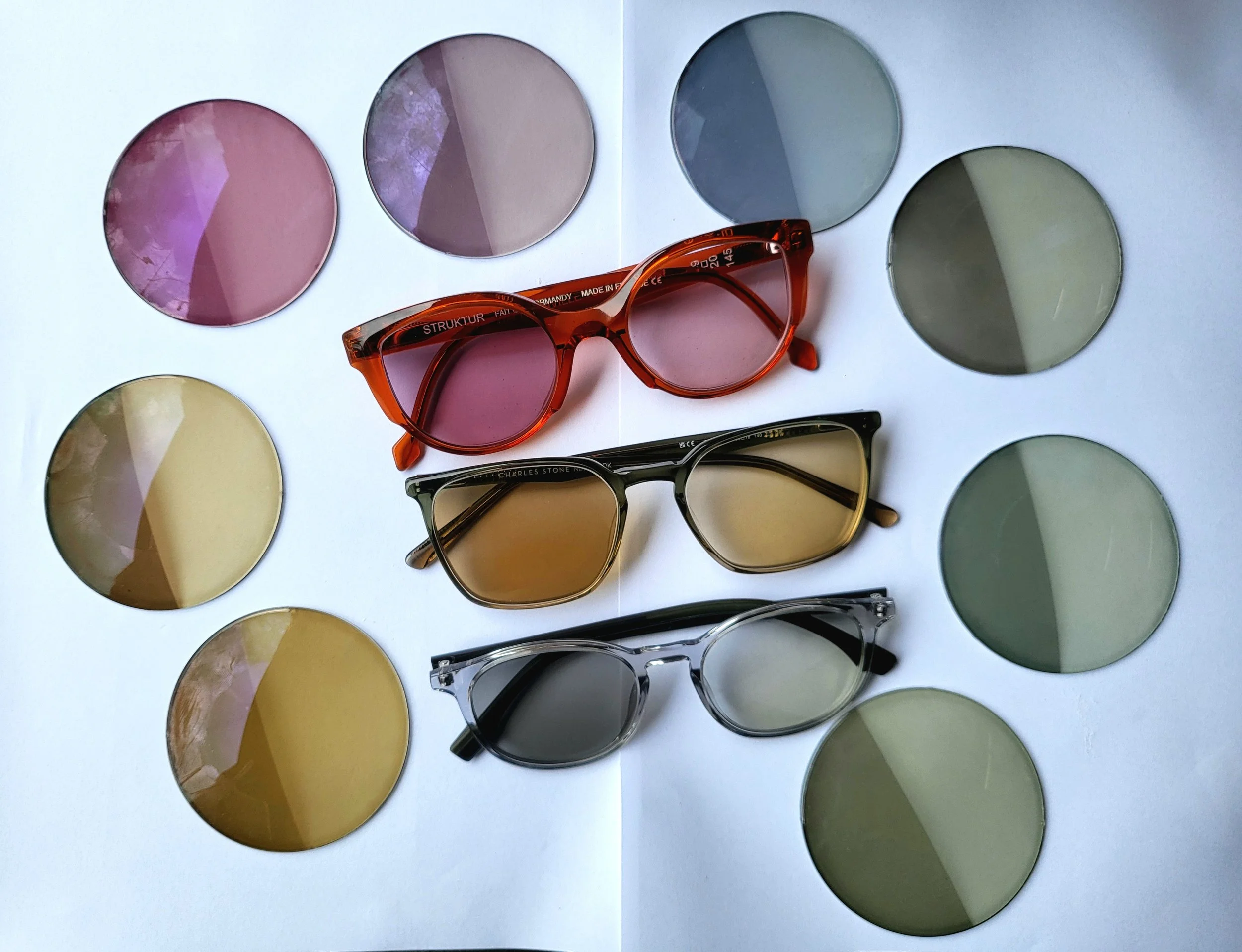 A variety of sunglasses with different tinted lenses arranged on a white surface, with color palettes displayed next to each pair.