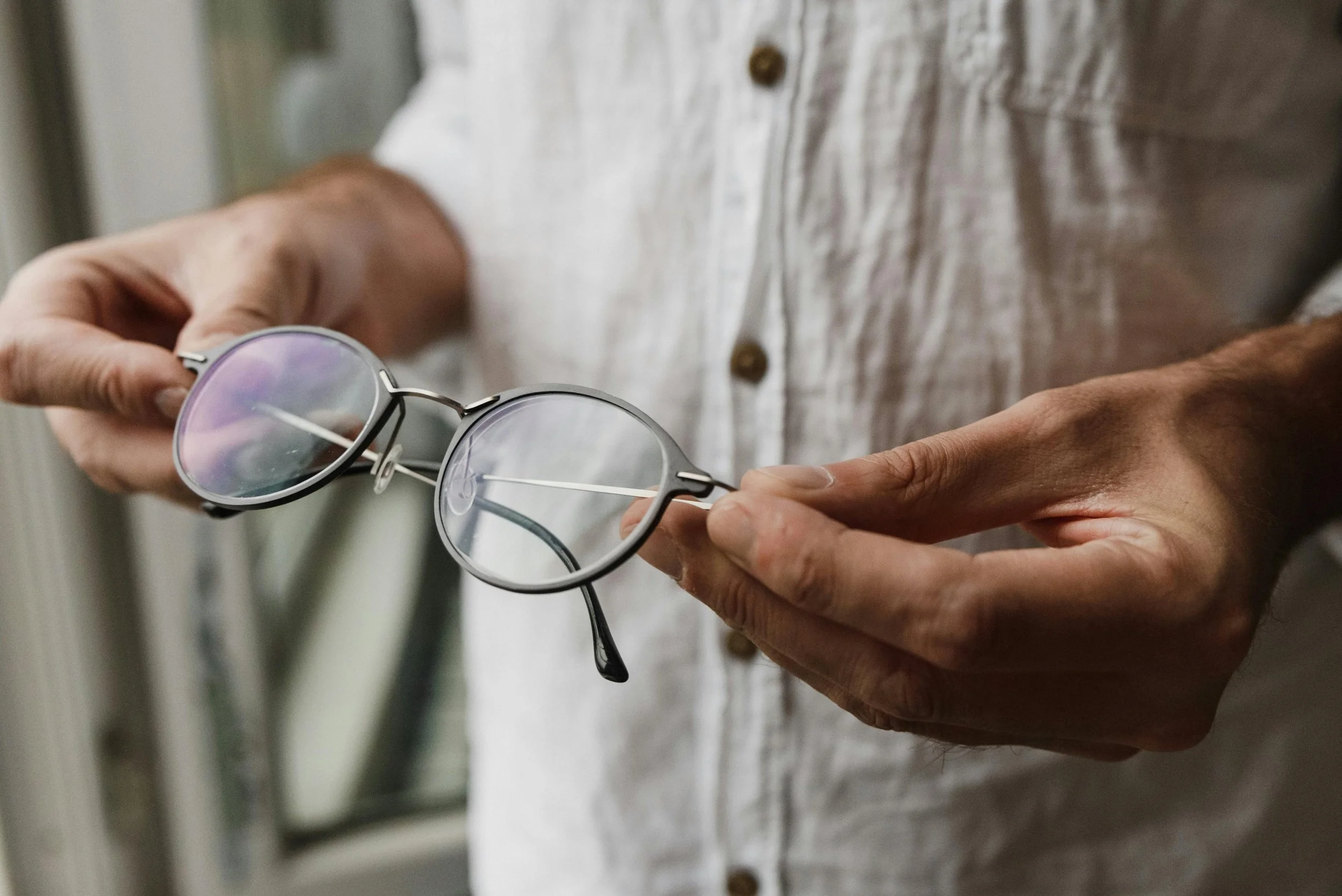 Close-up of a person holding a pair of sunglasses with a round frame and reflective lenses.