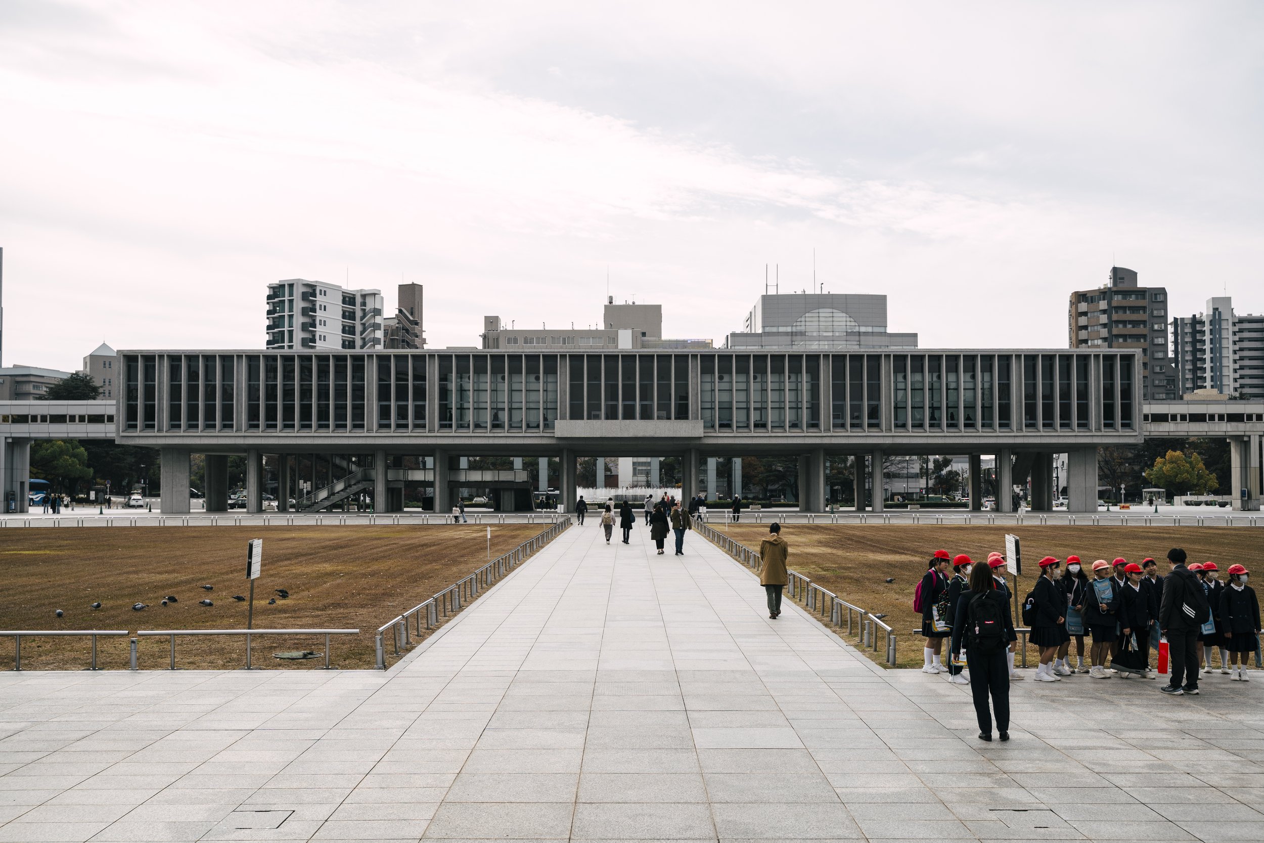 The Hiroshima Peace Memorial Museum stretches across the park grounds, flanked by schoolchildren on a field visit.