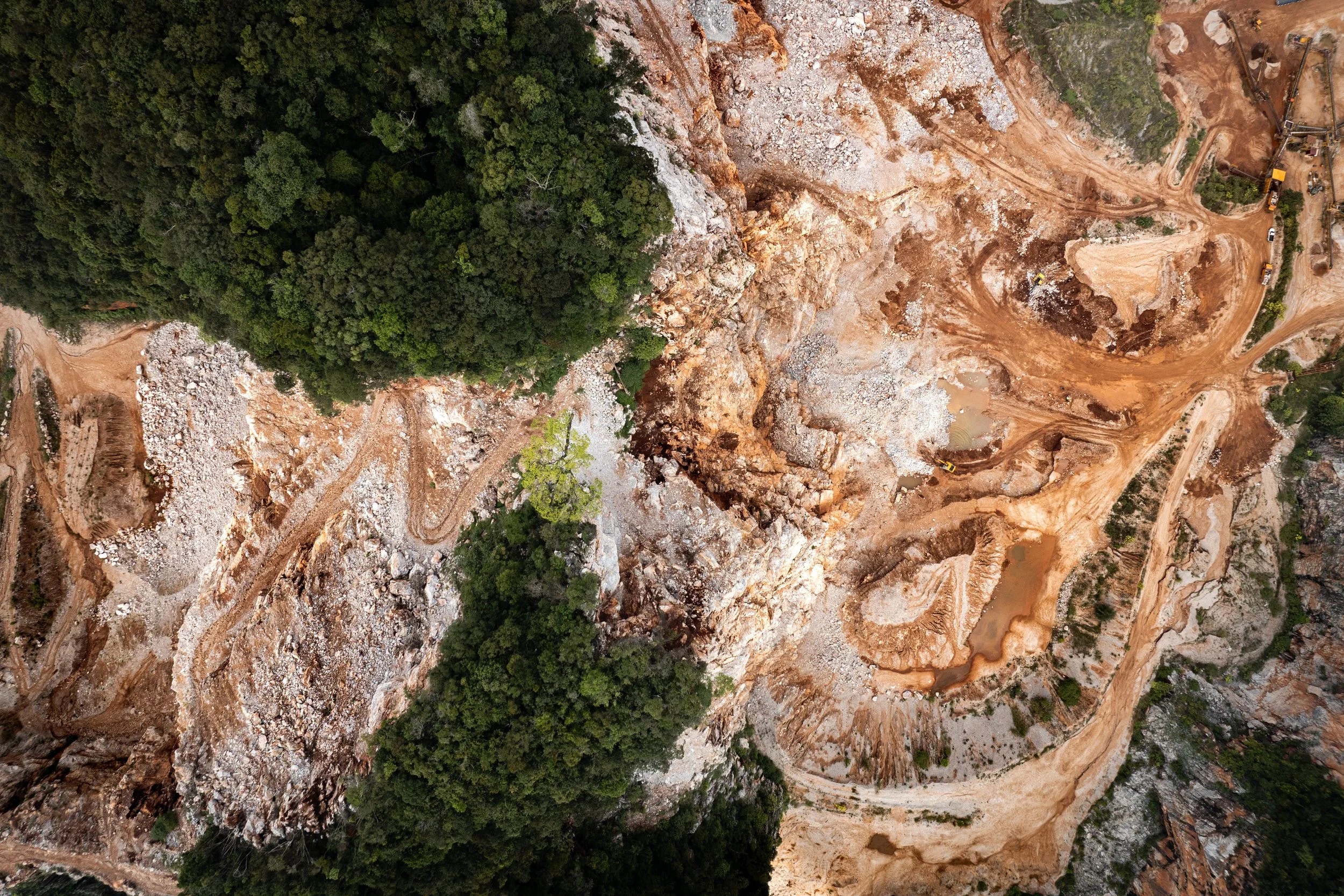 Top-down aerial view of an active limestone quarry in Perak, showing excavated terrain meeting the edge of remaining tropical rainforest.