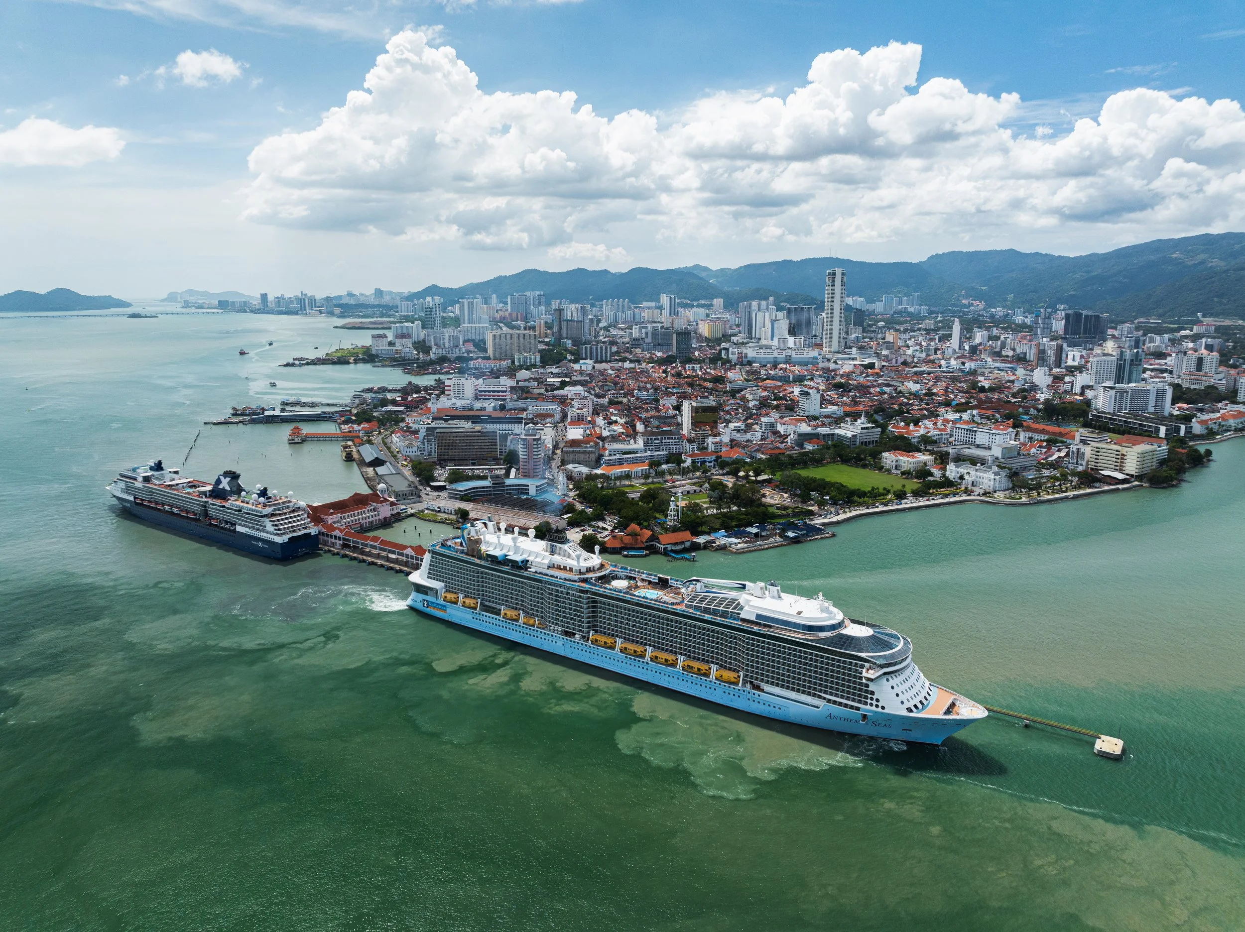 Swettenham Pier, Penang, Malaysia — Two cruise ships docked against the George Town waterfront, the heritage city spreading across the island behind them. The Strait of Malacca, still one of the world's busiest shipping lanes.