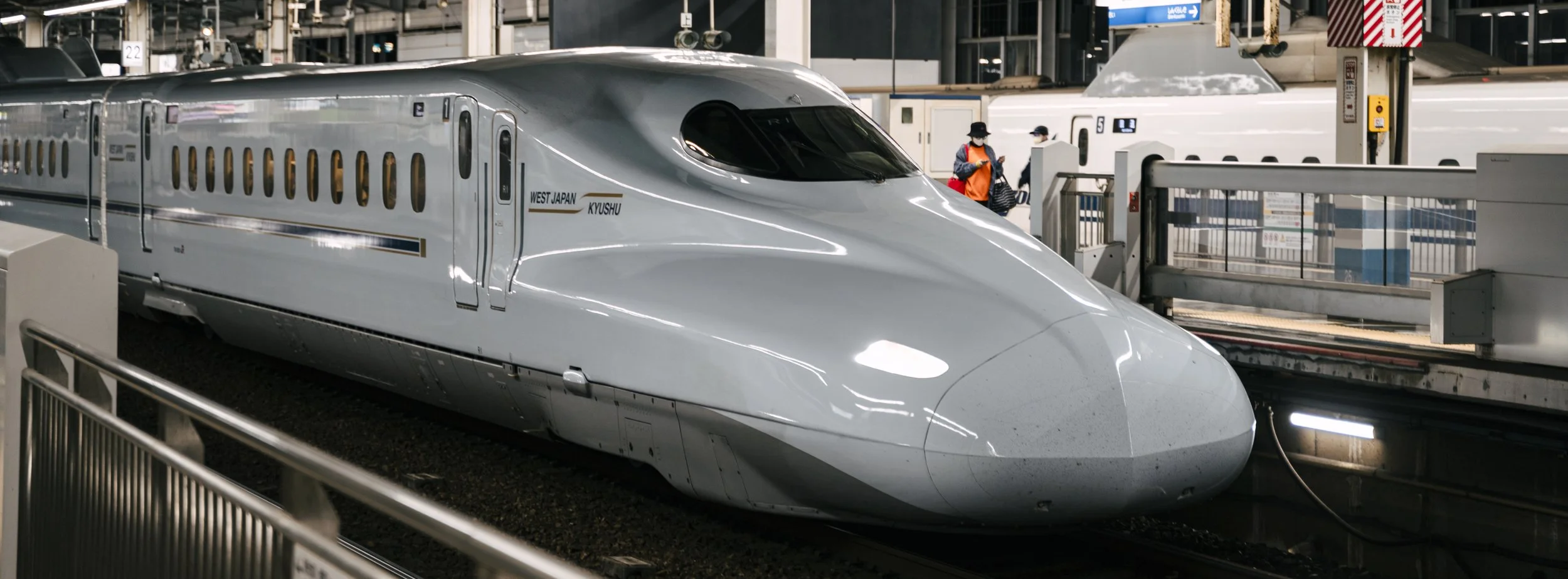 N700 Shinkansen (West Japan · Kyushu), Japan — Golden hour catches the nose of the N700 at the platform, the warm light tracing the curve of its aerodynamic shell. The mundane choreography of Japanese rail — precise, quietly beautiful.