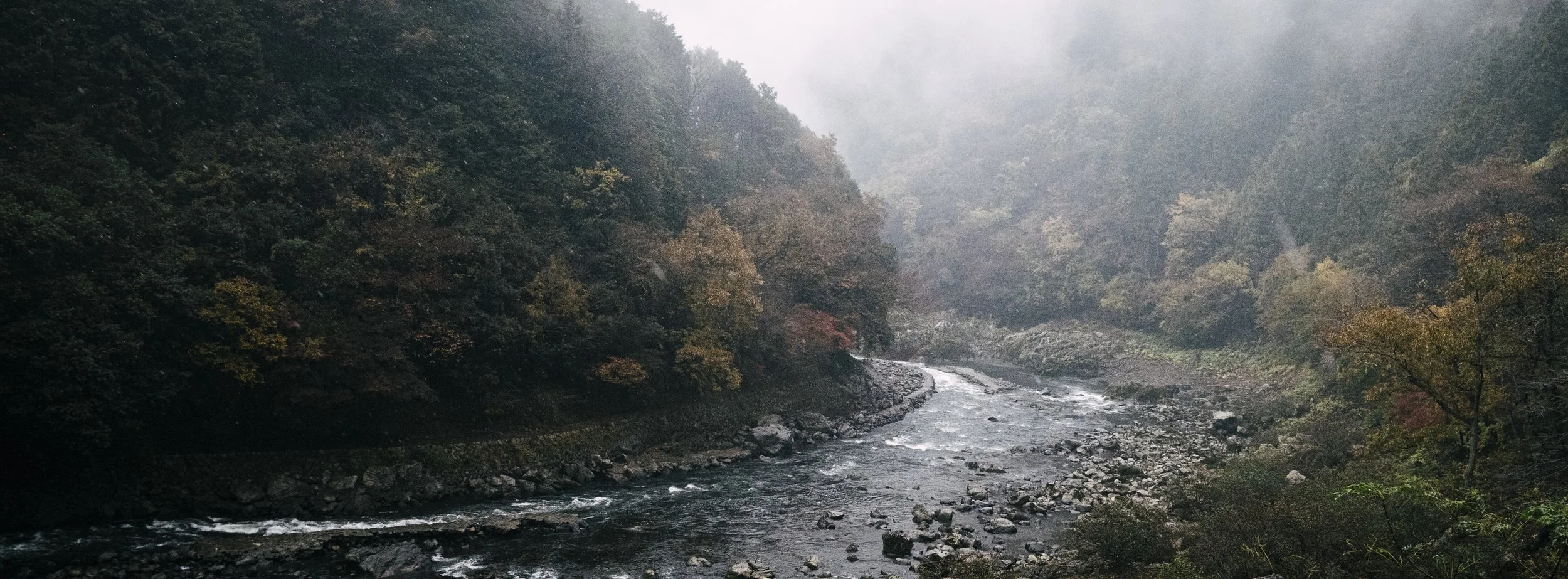 Hozugawa River, Arashiyama, Kyoto — The river curves through the gorge under low cloud and mist, autumn colour bleeding into the hillsides. 