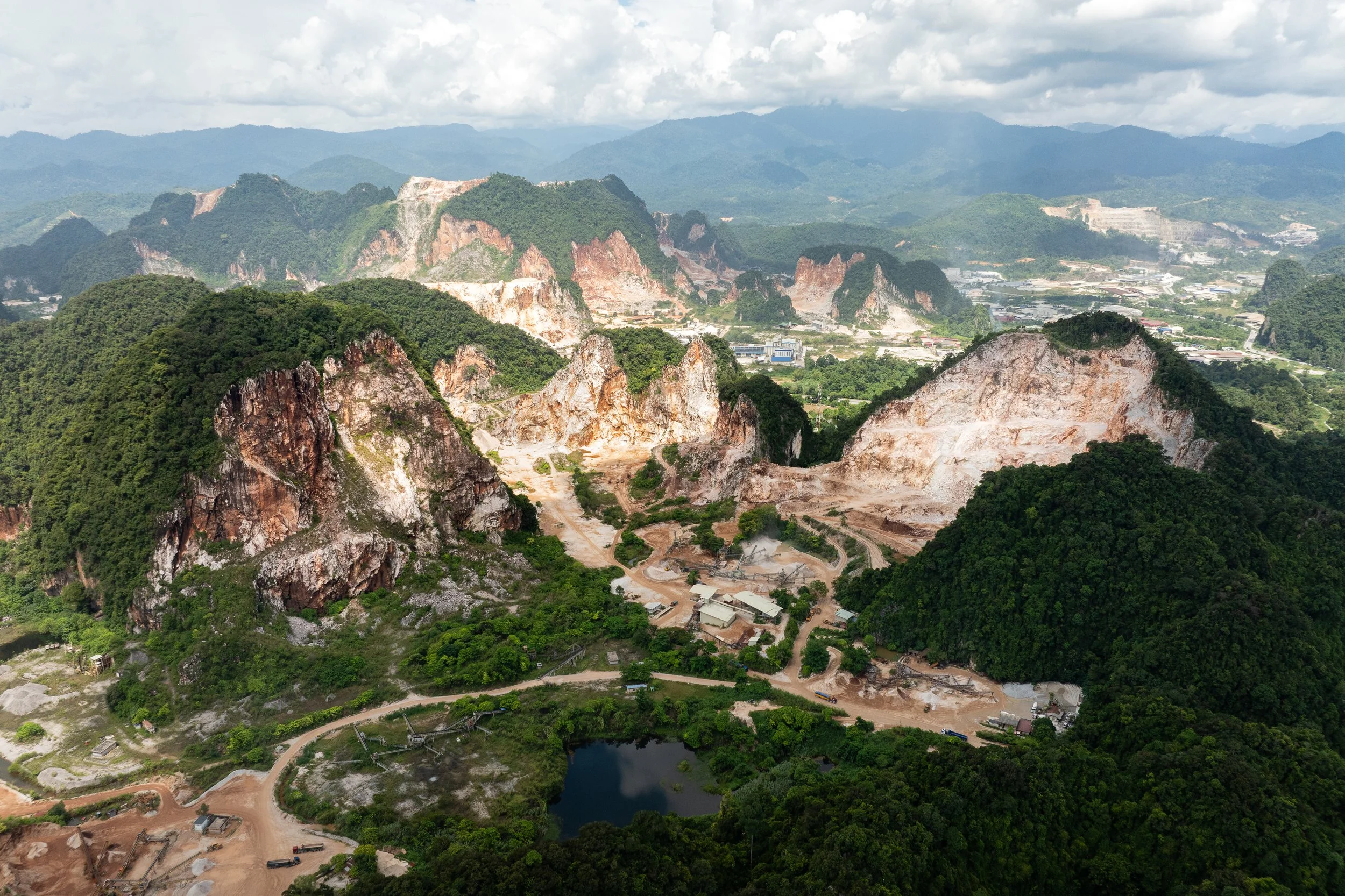 Aerial view of heavily quarried limestone hills surrounded by tropical jungle and industrial facilities in Simpang Pulai, Perak.