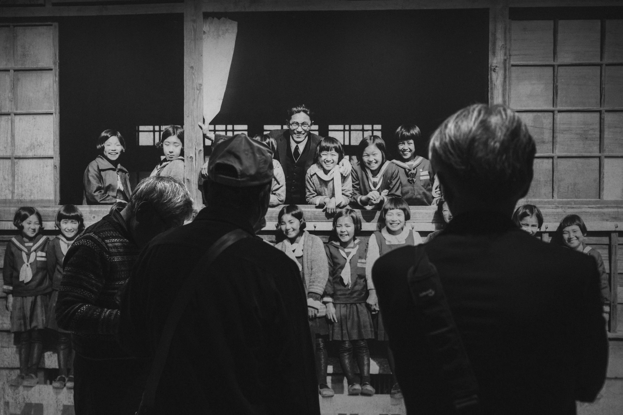Museum visitors pause before a wartime photograph of smiling Japanese schoolgirls and their teacher, a reminder of lives lost.